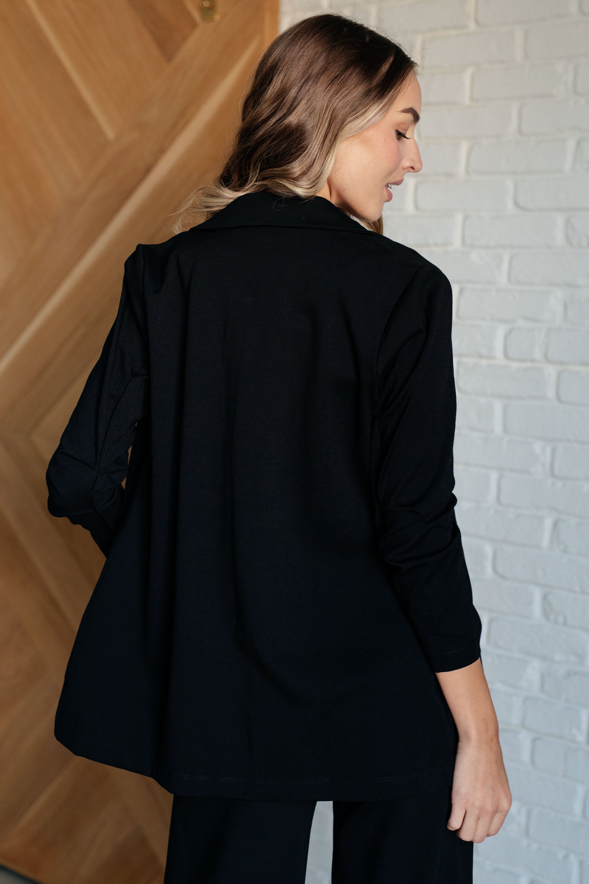 Black blazer with ruched 3/4 sleeves, open front, and notched lapel. Made from ponte knit with side pockets and a slim fit.