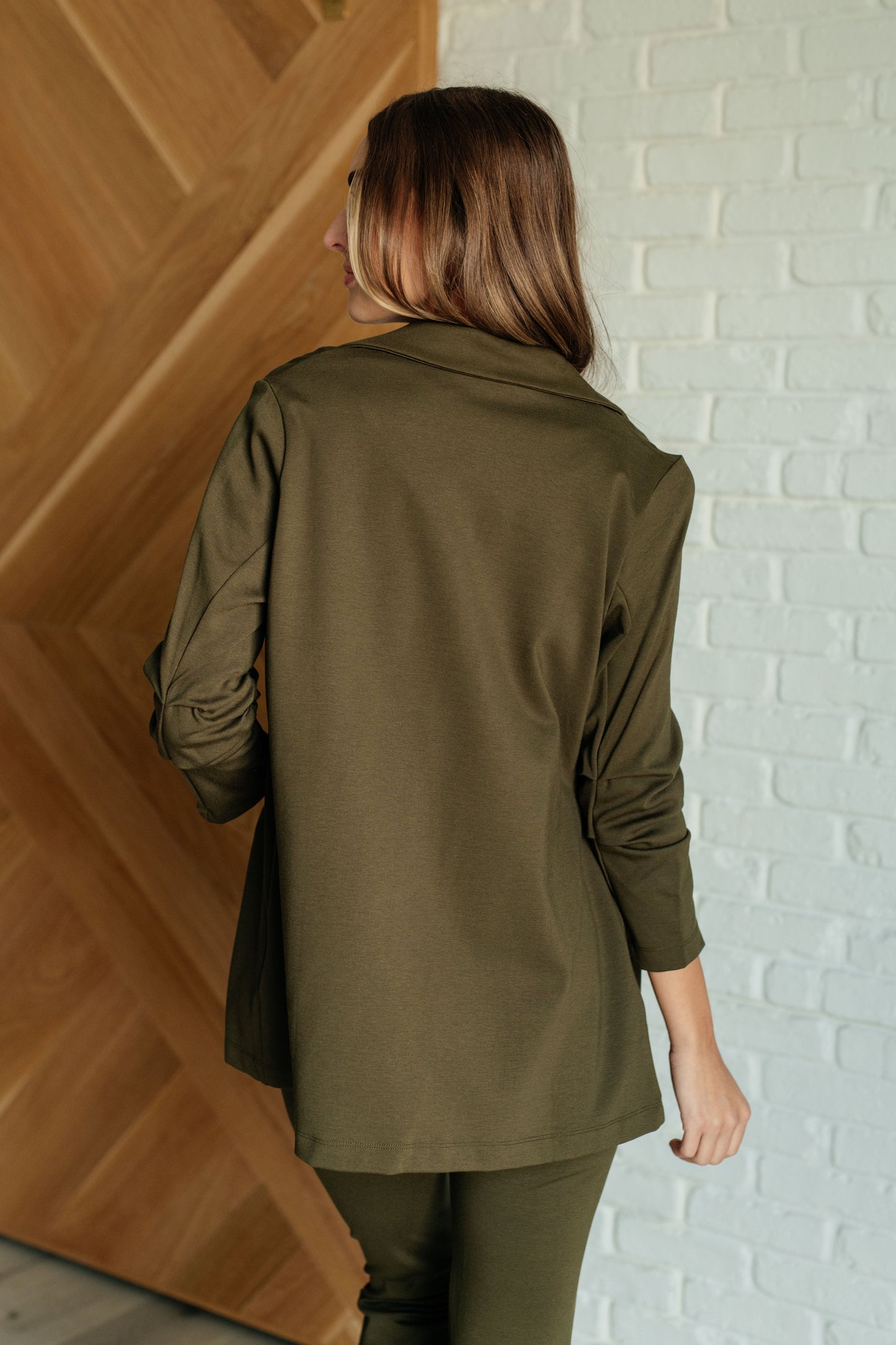 Olive-colored blazer with ruched 3/4 sleeves, open front, and notched lapel. Made from ponte knit with side pockets and a slim fit.