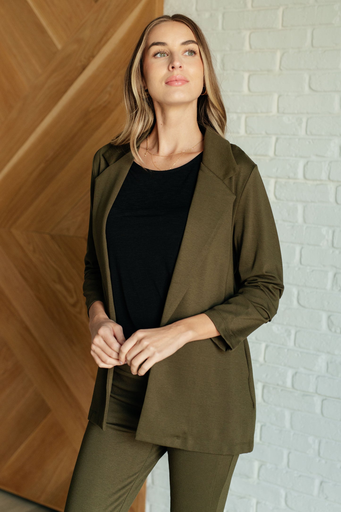 Olive-colored blazer with ruched 3/4 sleeves, open front, and notched lapel. Made from ponte knit with side pockets and a slim fit.