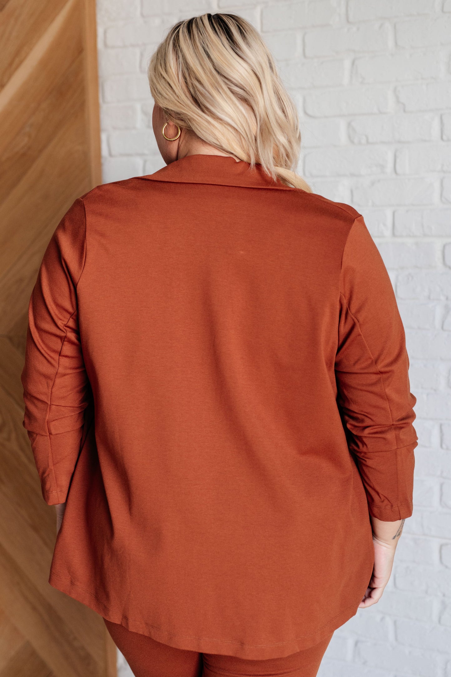 Rust-colored blazer with ruched 3/4 sleeves, open front, and notched lapel. Made from ponte knit with side pockets and a slim fit.