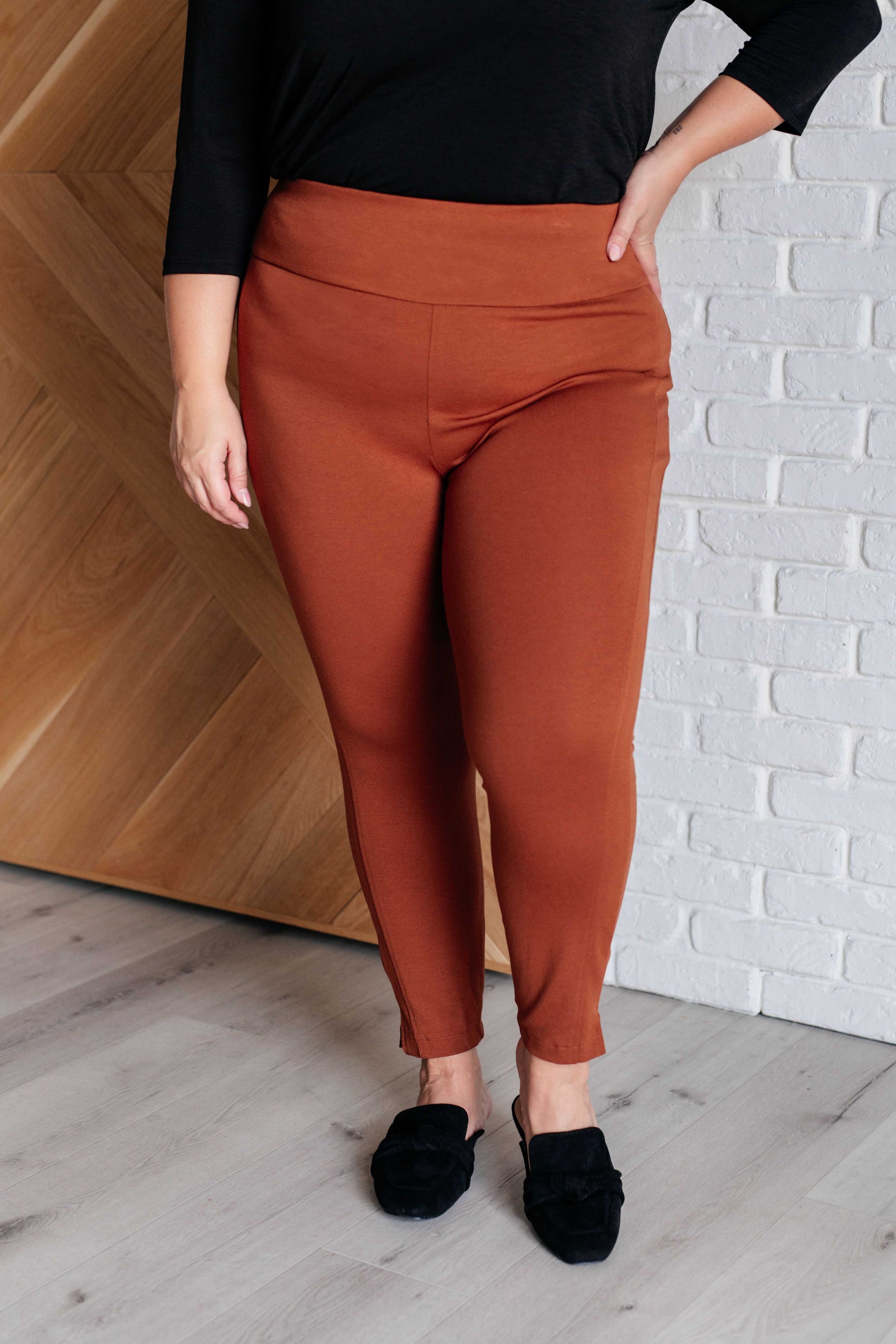 Skinny Pants in rust, high-rise, slim-fit, made from ponte knit fabric. Pull-on style with tuxedo stripe, faux welt pockets, and cuff slit. Ankle crop design for a chic, flattering look