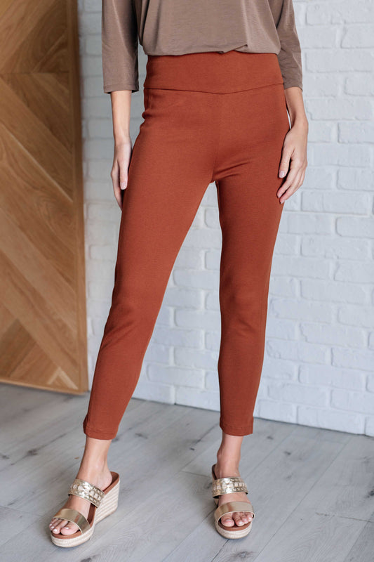 Skinny Pants in rust, high-rise, slim-fit, made from ponte knit fabric. Pull-on style with tuxedo stripe, faux welt pockets, and cuff slit. Ankle crop design for a chic, flattering look