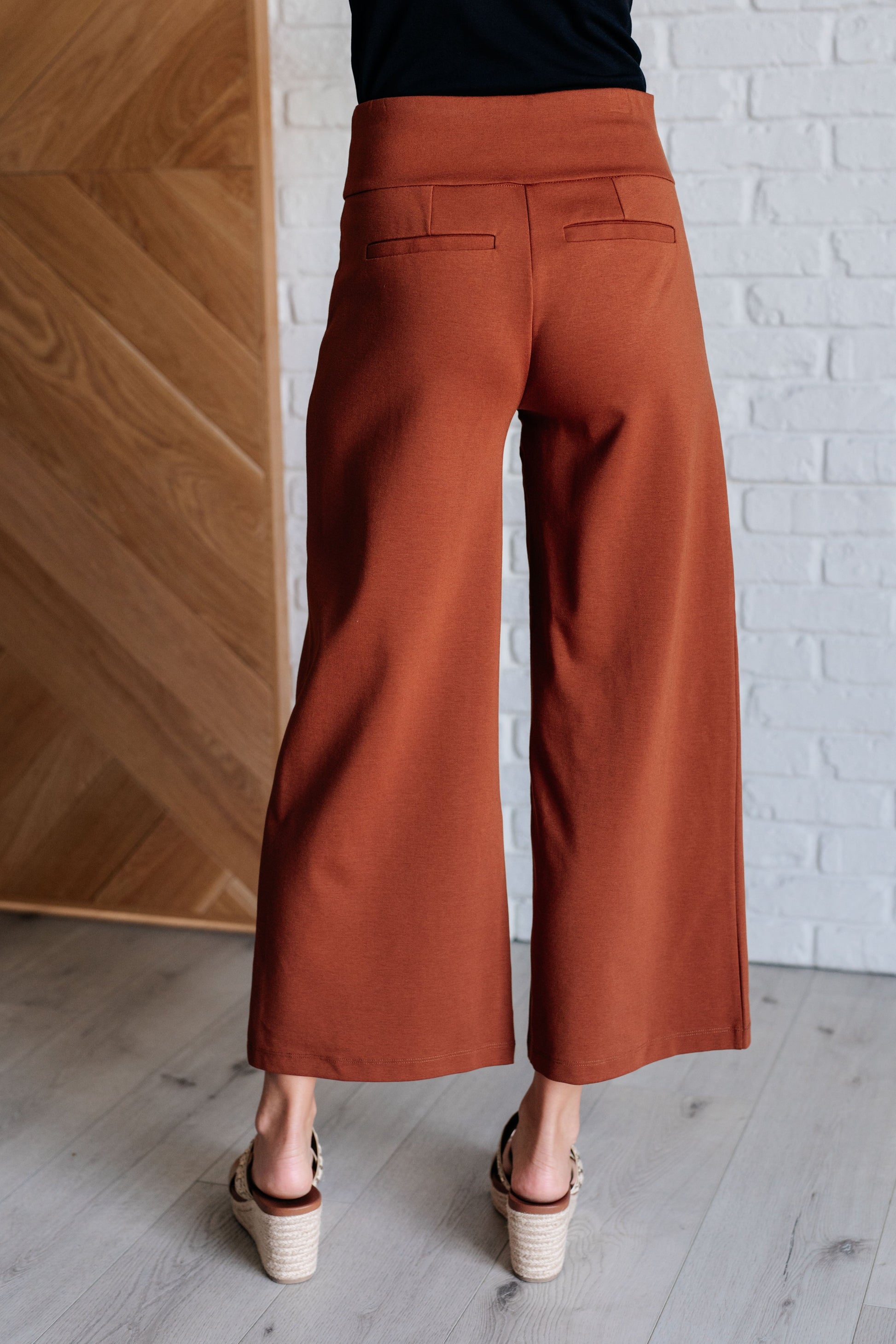 Wide Leg Crop Pants in rust, made from high-stretch ponte knit fabric. Cropped, wide-leg design with faux welt pocket. Perfect for effortless style.