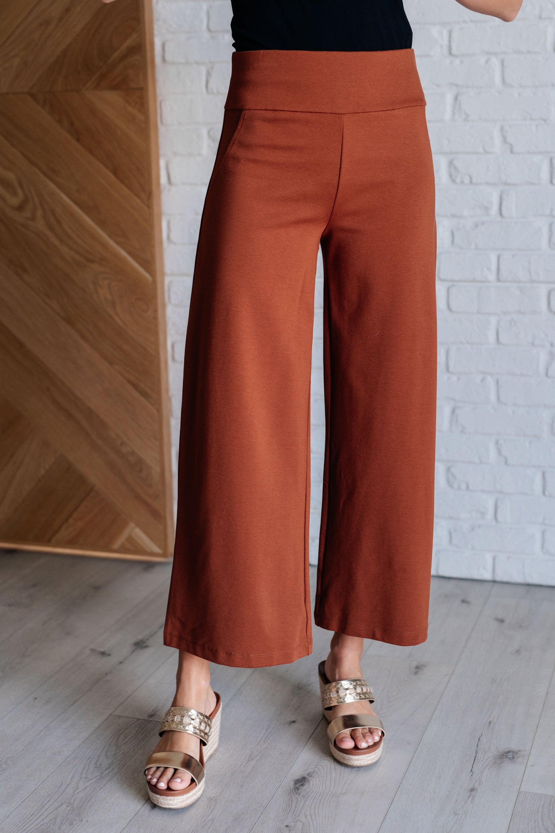 Wide Leg Crop Pants in rust, made from high-stretch ponte knit fabric. Cropped, wide-leg design with faux welt pocket. Perfect for effortless style.