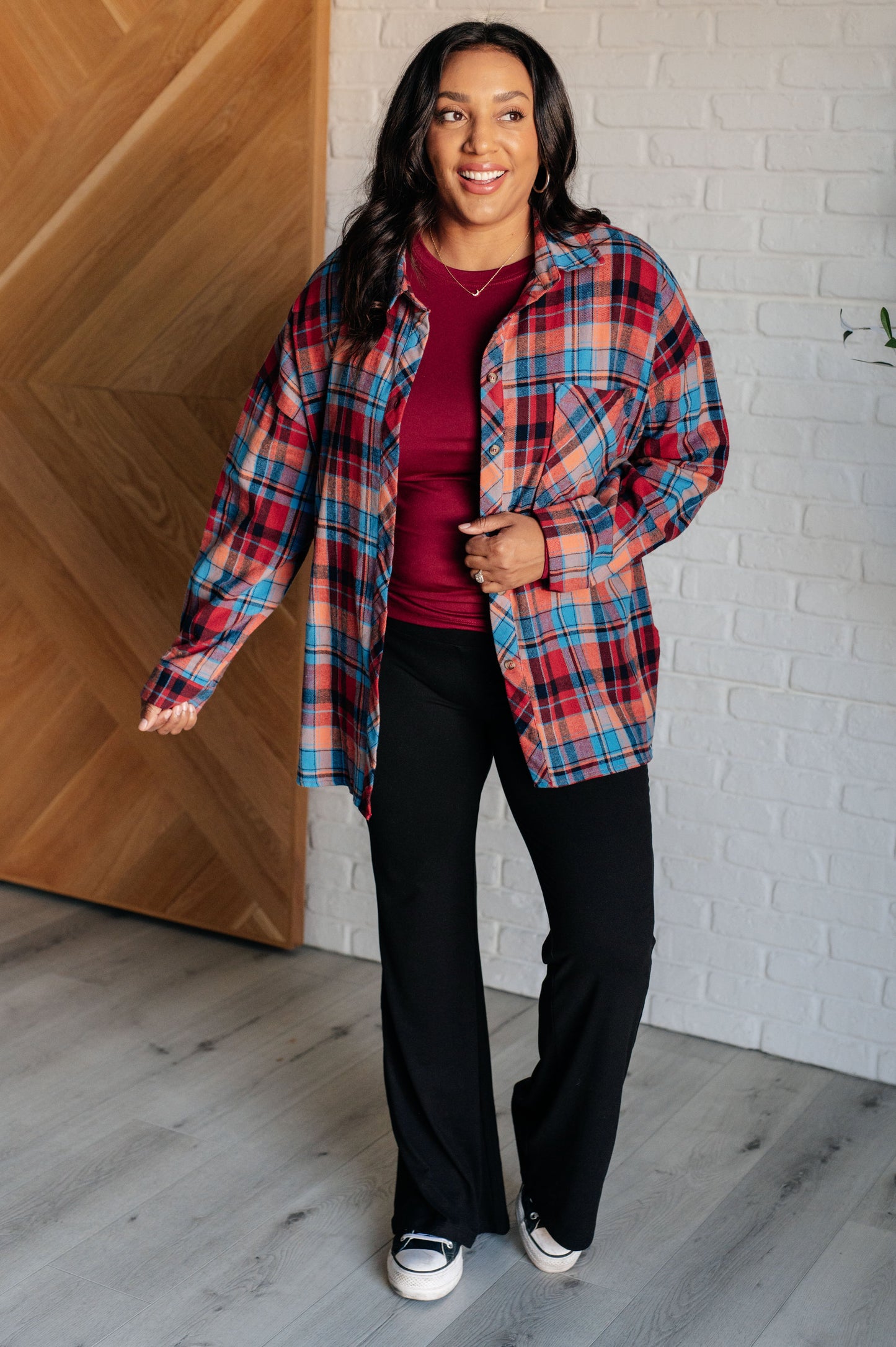 Blue and red plaid flannel button-up shirt with a collared neckline, drop shoulders, and chest patch pocket. Features buttoned sleeve cuffs, scooped hem, and side slits.