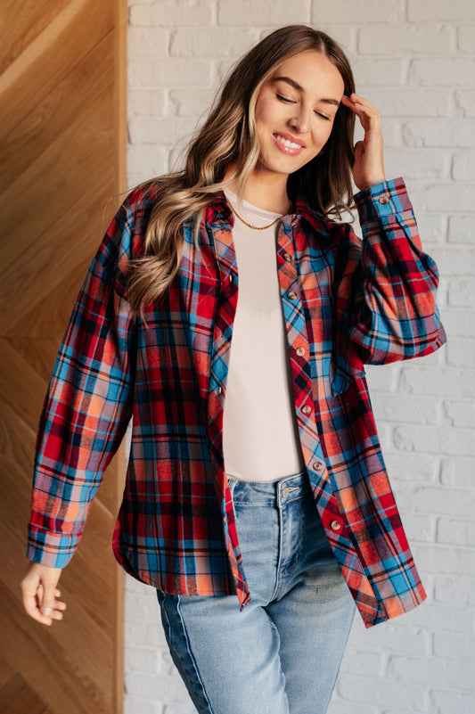 Blue and red plaid flannel button-up shirt with a collared neckline, drop shoulders, and chest patch pocket. Features buttoned sleeve cuffs, scooped hem, and side slits.