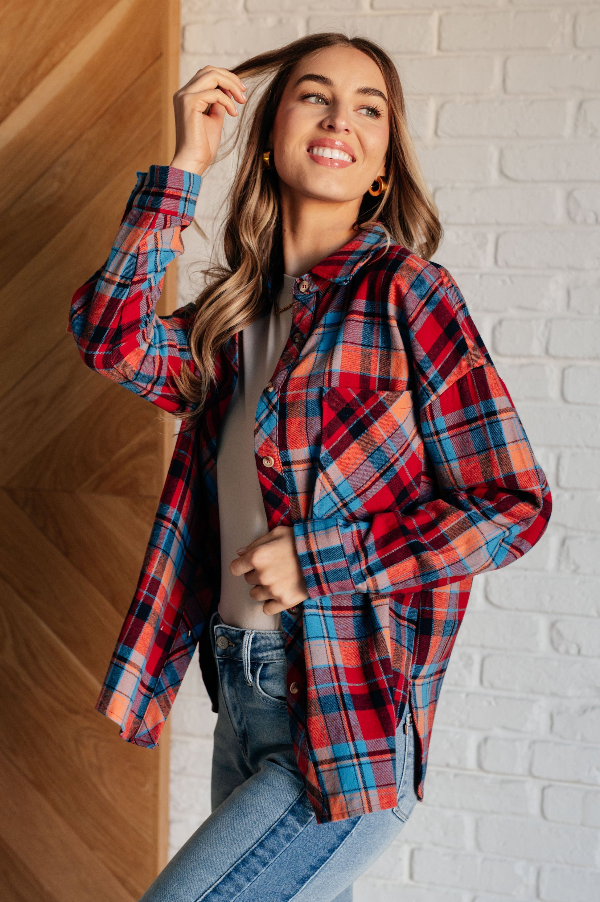 Blue and red plaid flannel button-up shirt with a collared neckline, drop shoulders, and chest patch pocket. Features buttoned sleeve cuffs, scooped hem, and side slits.