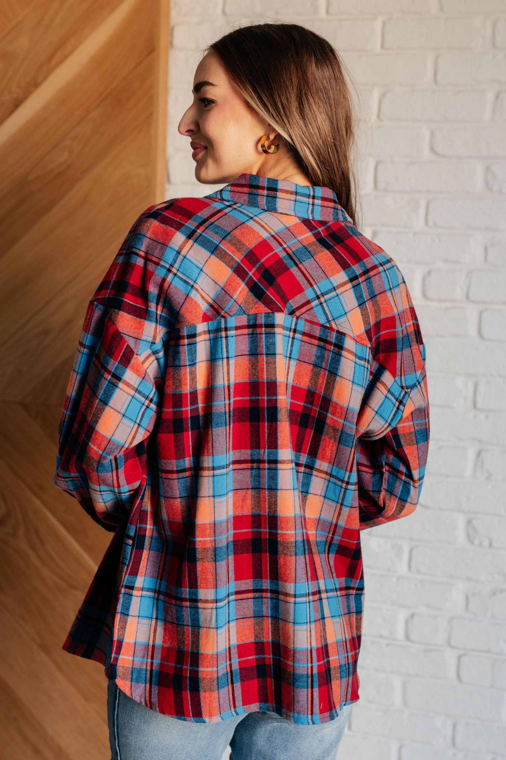 Blue and red plaid flannel button-up shirt with a collared neckline, drop shoulders, and chest patch pocket. Features buttoned sleeve cuffs, scooped hem, and side slits.