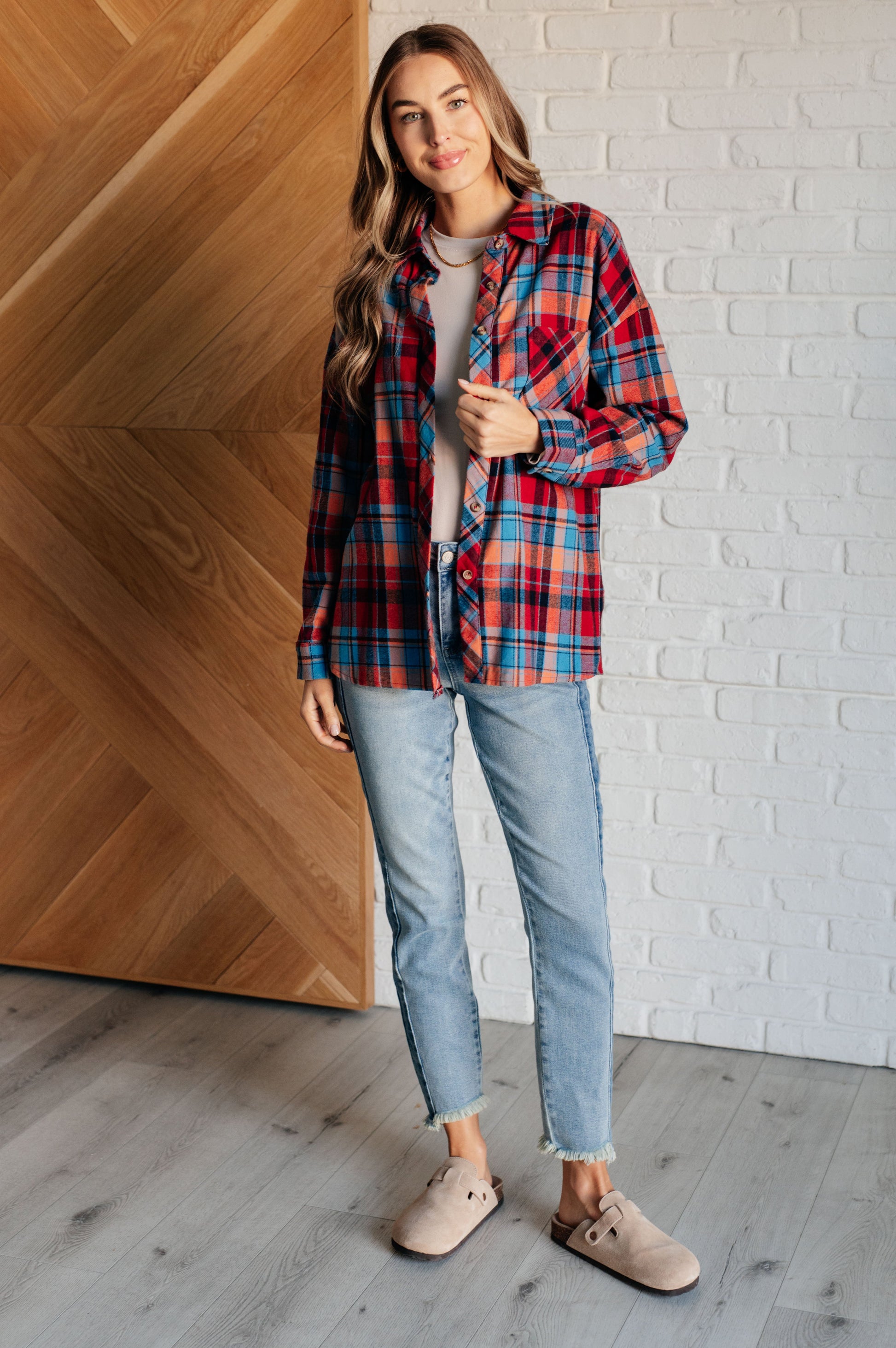 Blue and red plaid flannel button-up shirt with a collared neckline, drop shoulders, and chest patch pocket. Features buttoned sleeve cuffs, scooped hem, and side slits.