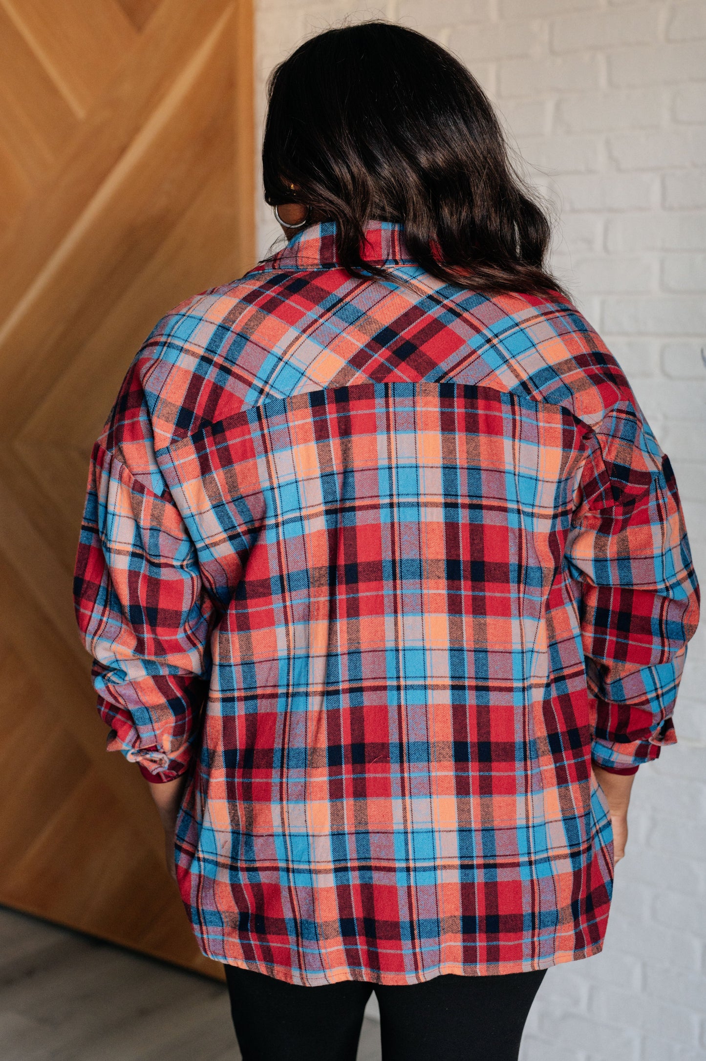 Blue and red plaid flannel button-up shirt with a collared neckline, drop shoulders, and chest patch pocket. Features buttoned sleeve cuffs, scooped hem, and side slits.