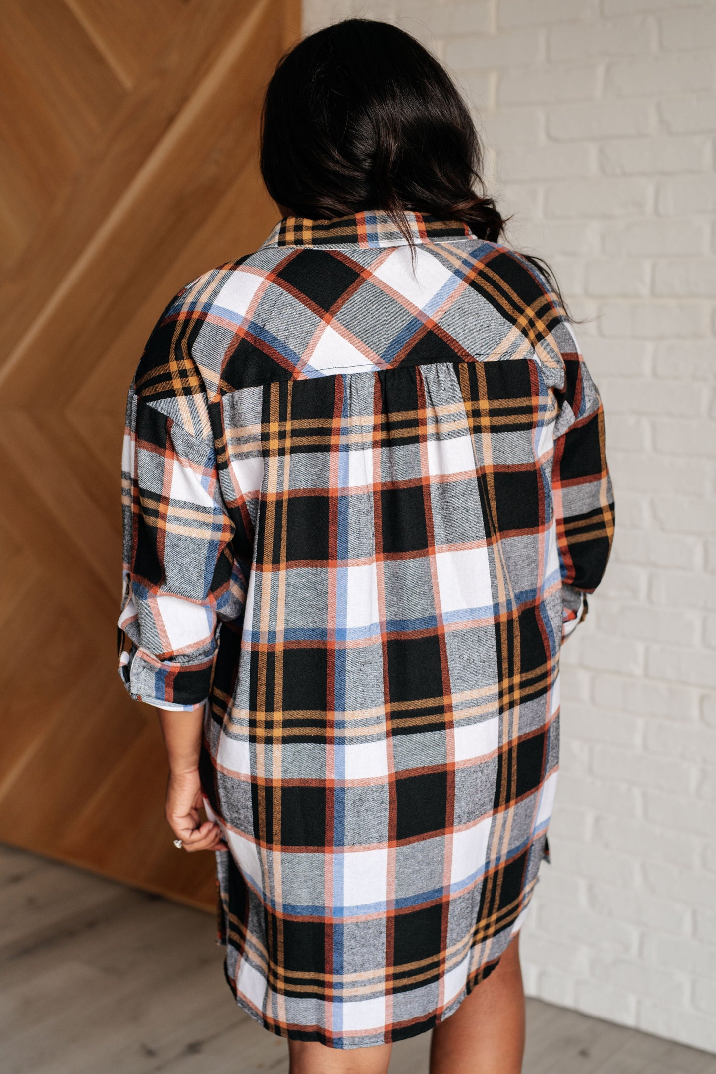 Black plaid flannel shirt dress with a collared neckline, button front closure, and long sleeves with roll button tabs. and side slits.