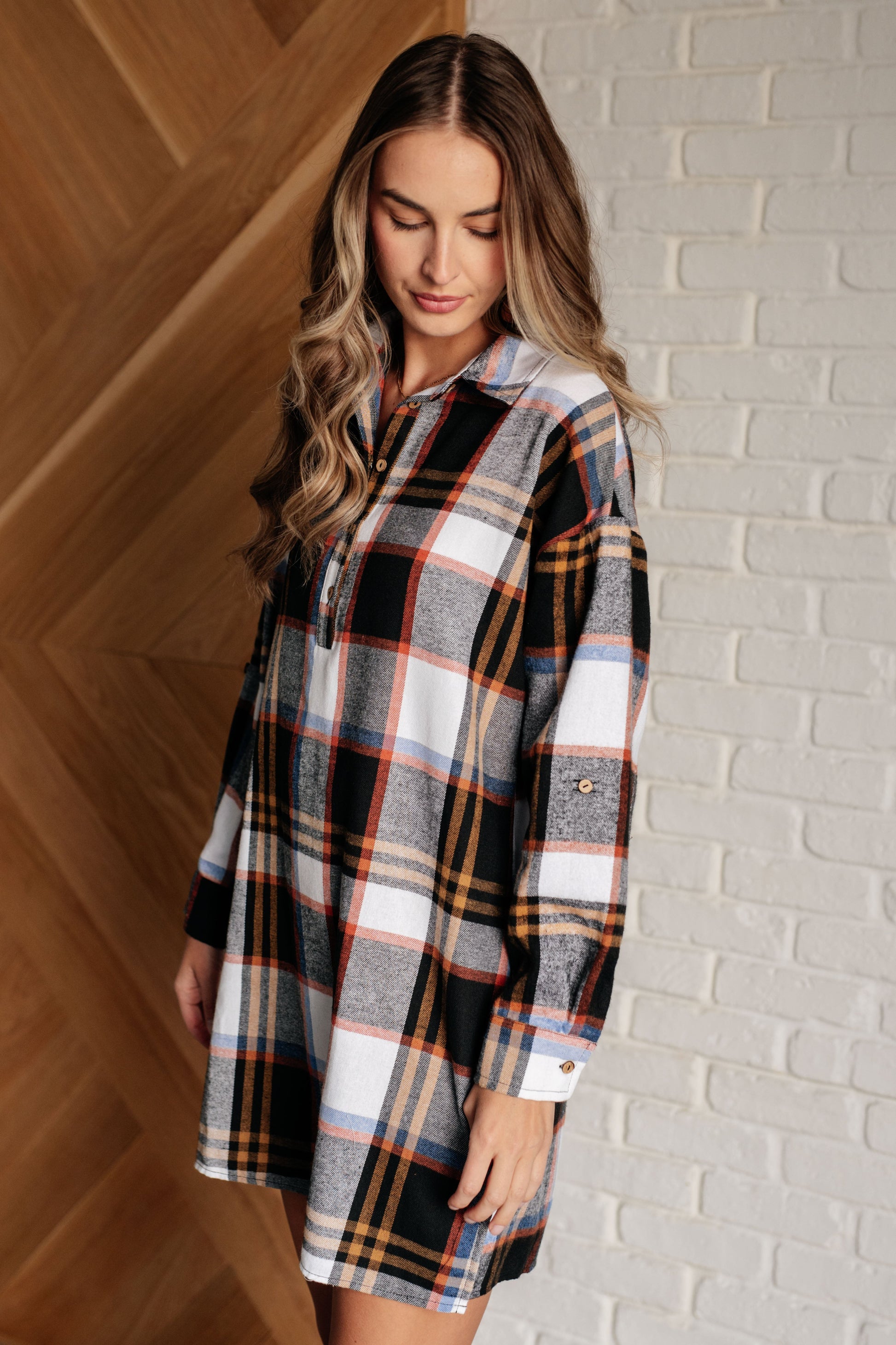 Black plaid flannel shirt dress with a collared neckline, button front closure, and long sleeves with roll button tabs. and side slits.