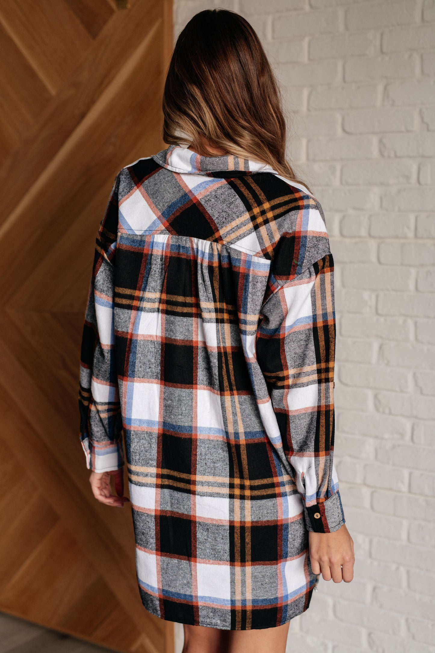 Black plaid flannel shirt dress with a collared neckline, button front closure, and long sleeves with roll button tabs. and side slits.