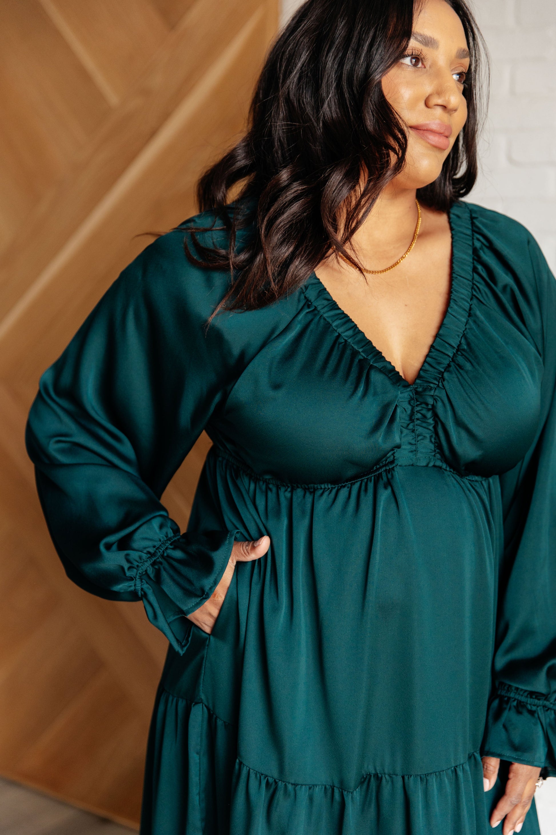 Hunter green poly satin tiered dress with V-neck, long balloon sleeves, and elastic at the neck, shoulders, and sleeve cuffs. Elastic empire waist and functional side pockets.