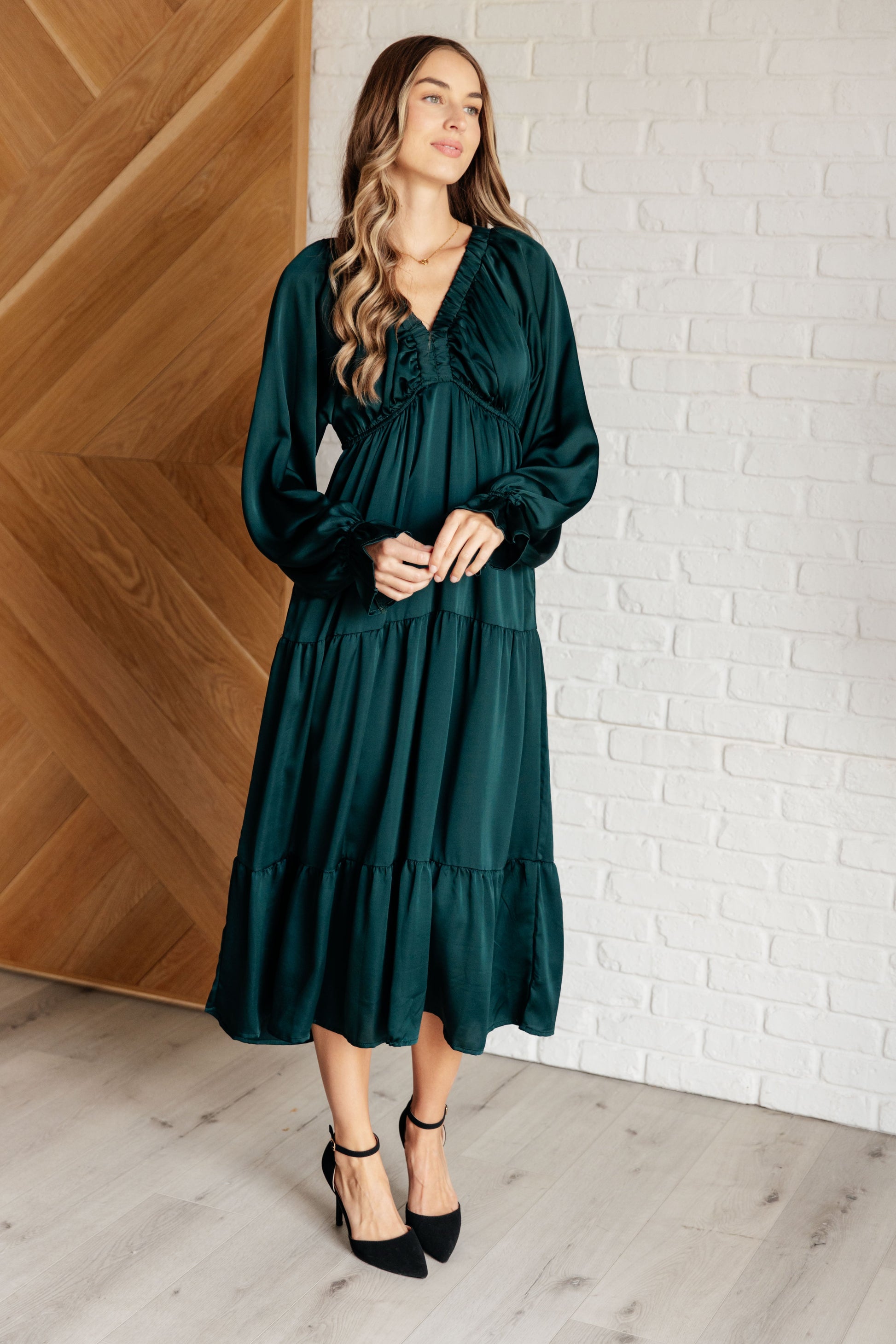 Hunter green poly satin tiered dress with V-neck, long balloon sleeves, and elastic at the neck, shoulders, and sleeve cuffs. Elastic empire waist and functional side pockets.