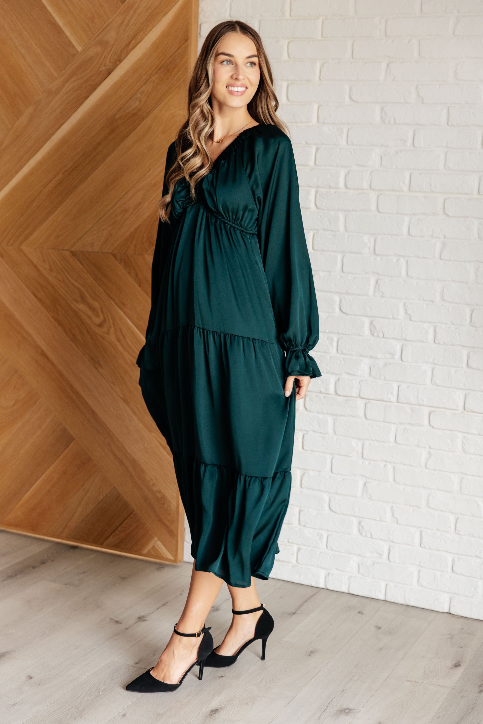 Hunter green poly satin tiered dress with V-neck, long balloon sleeves, and elastic at the neck, shoulders, and sleeve cuffs. Elastic empire waist and functional side pockets.