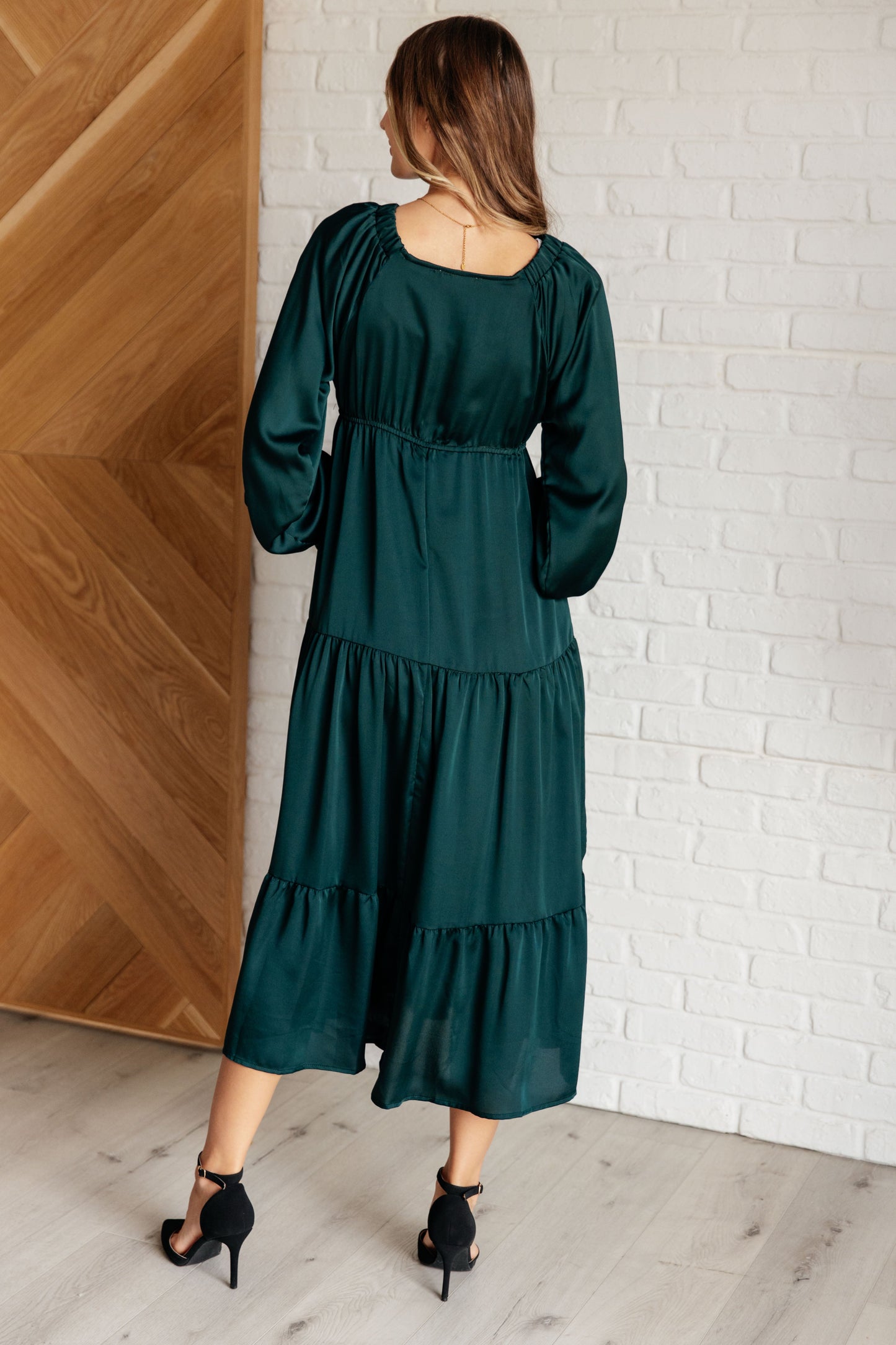 Hunter green poly satin tiered dress with V-neck, long balloon sleeves, and elastic at the neck, shoulders, and sleeve cuffs. Elastic empire waist and functional side pockets.