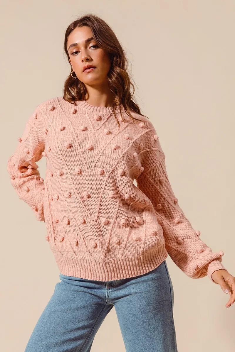 Full body view of model wearing blush pom pom textured knit sweater with jeans for casual chic.