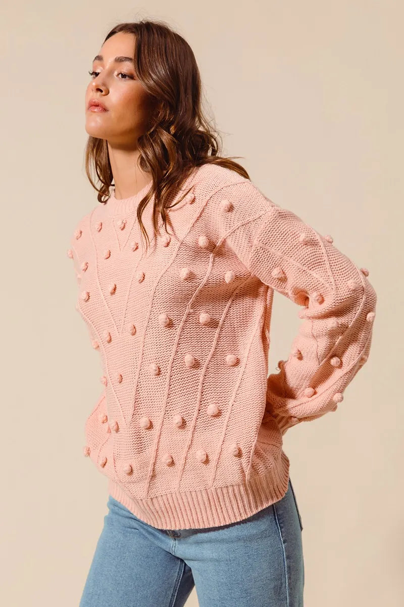 Side angle of blush pom pom knit sweater top with cozy ribbed texture and long sleeves for fall style.