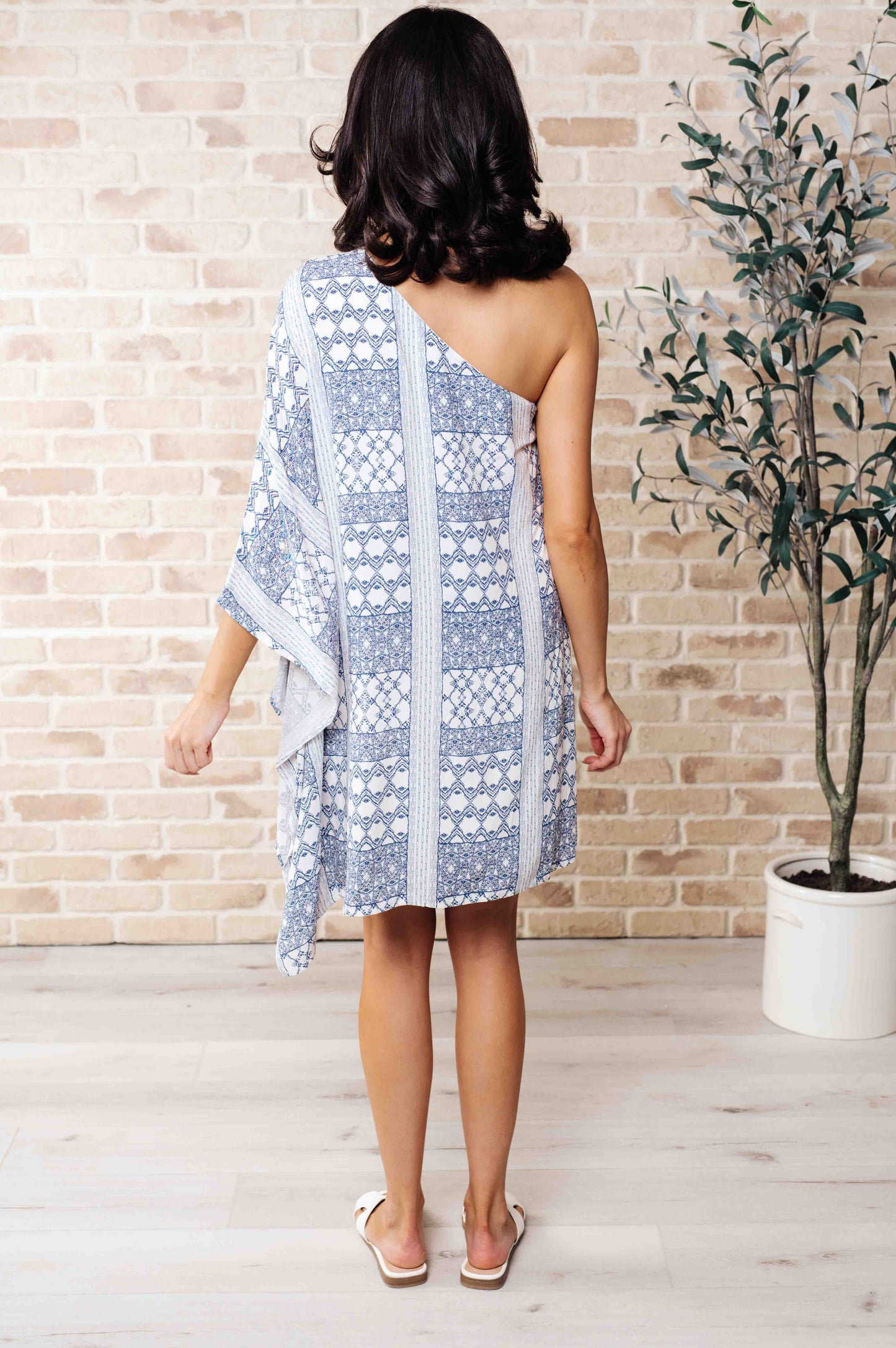 Back view of model in Marjorie One Shoulder Blue Dress with contrasting print, draped neckline, and chic shift silhouette.