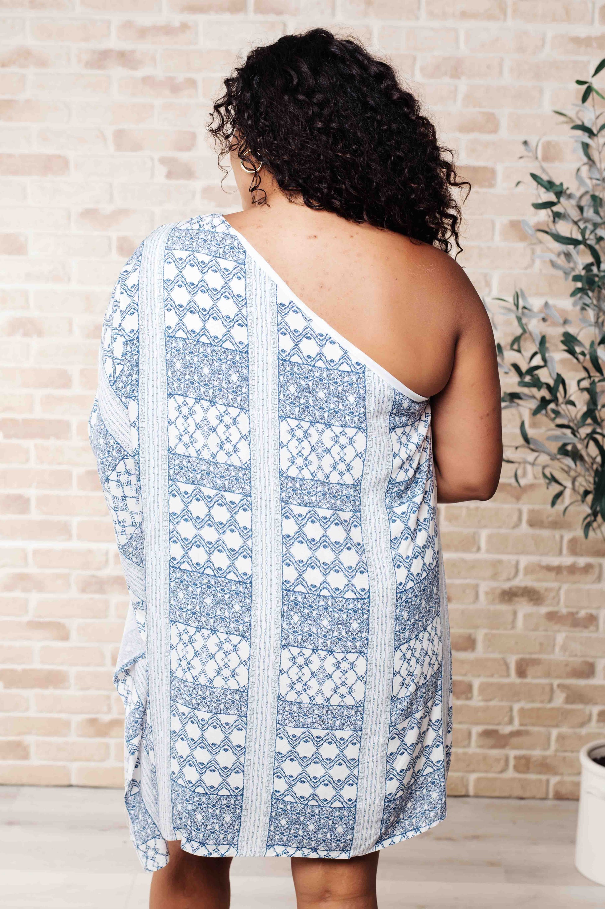 Back view of plus size model in Marjorie One Shoulder Blue Dress with contrasting print, draped neckline, and shift silhouette.