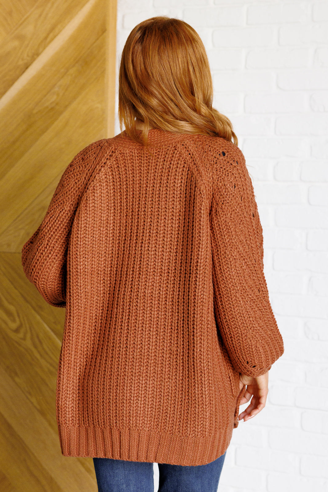 Women's long-line cardigan in chestnut sweater knit fabric with an open front, long sleeves, functional patch pockets, and exaggerated ribbed sleeve cuffs and hemline.