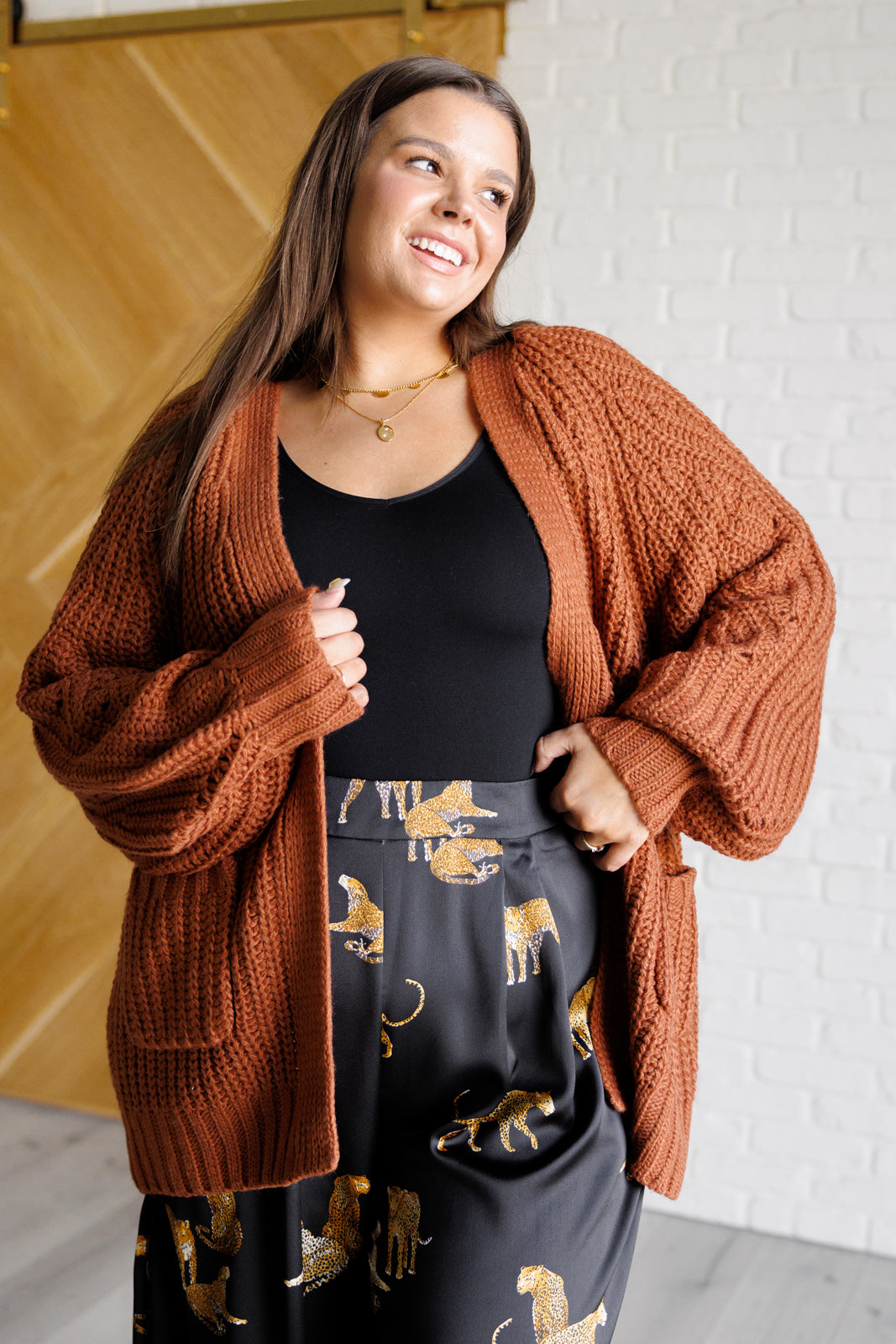 Women's long-line cardigan in chestnut sweater knit fabric with an open front, long sleeves, functional patch pockets, and exaggerated ribbed sleeve cuffs and hemline.