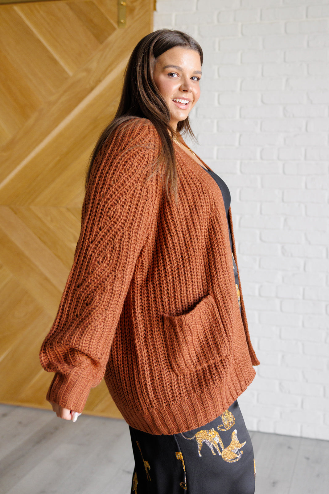 Women's long-line cardigan in chestnut sweater knit fabric with an open front, long sleeves, functional patch pockets, and exaggerated ribbed sleeve cuffs and hemline.