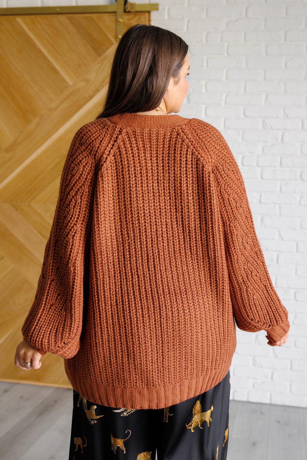 Women's long-line cardigan in chestnut sweater knit fabric with an open front, long sleeves, functional patch pockets, and exaggerated ribbed sleeve cuffs and hemline.