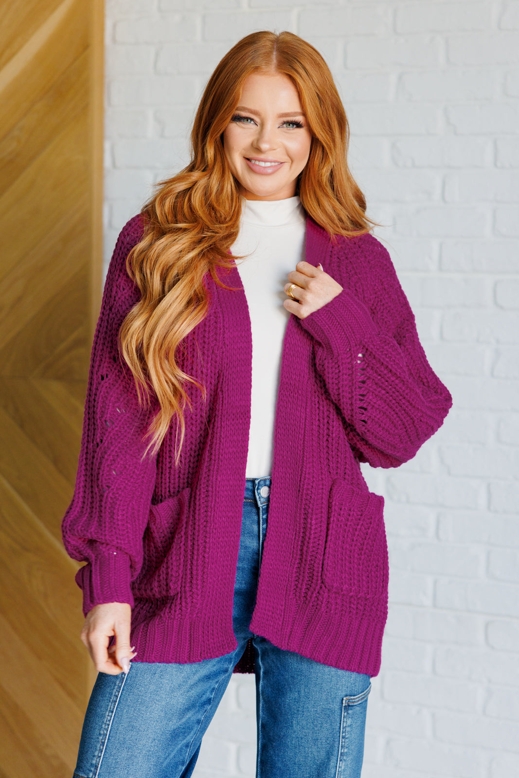 Women's long-line cardigan in the color berry sweater knit fabric with an open front, long sleeves, functional patch pockets, and exaggerated ribbed sleeve cuffs and hemline.