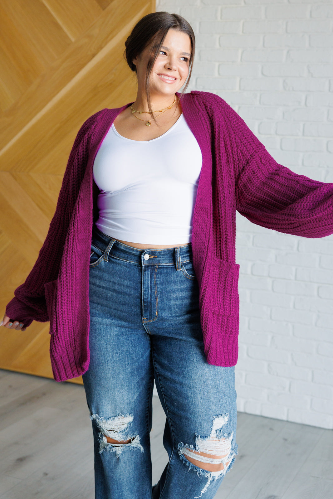 Women's long-line cardigan in the color berry sweater knit fabric with an open front, long sleeves, functional patch pockets, and exaggerated ribbed sleeve cuffs and hemline.