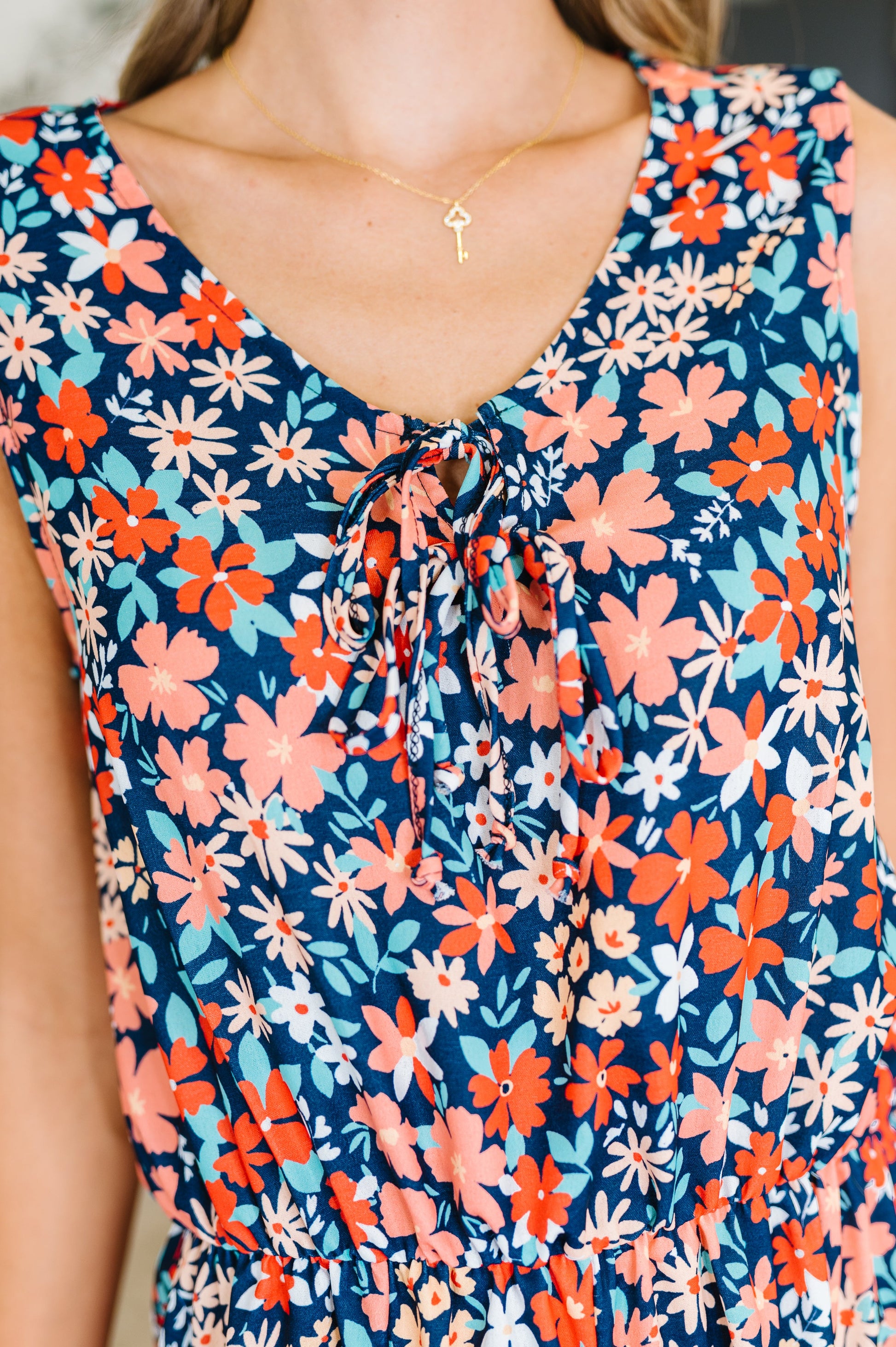 Close-up of Meadow romper showing tied neckline with bow detail, round collar, and navy floral print fabric.