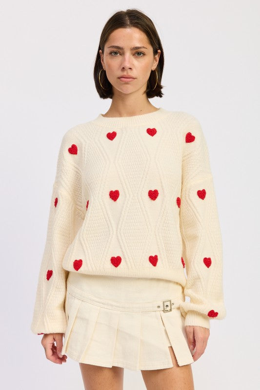 Model wearing Dana Embroidered Sweater in ivory with red heart embroidery.