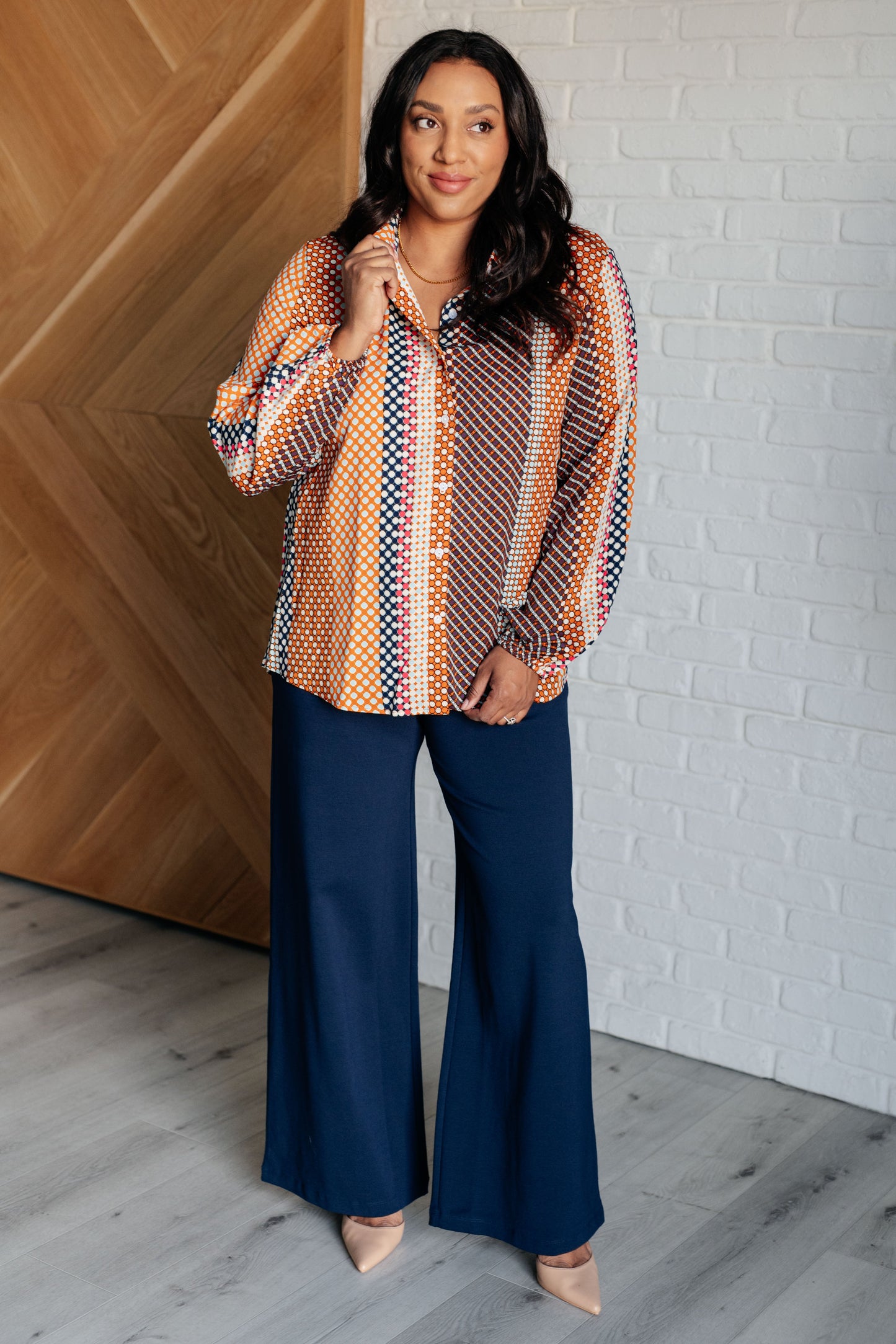 Navy, orange, brown, and pink polka dot poplin woven top with a collared neckline. Features long balloon sleeves with cased elastic cuffs, front button closures, and a scooped high-low hem.