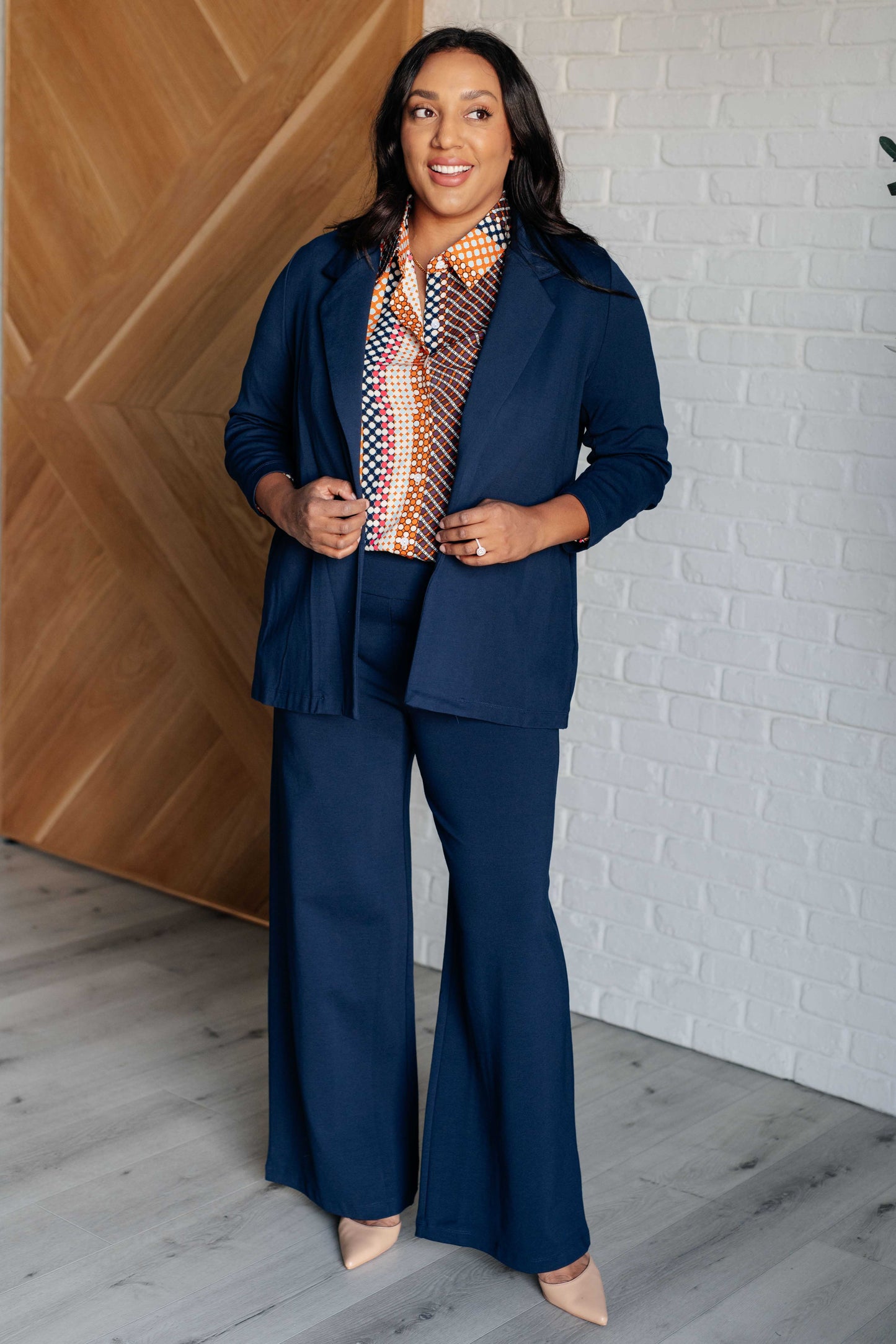 Navy, orange, brown, and pink polka dot poplin woven top with a collared neckline. Features long balloon sleeves with cased elastic cuffs, front button closures, and a scooped high-low hem.