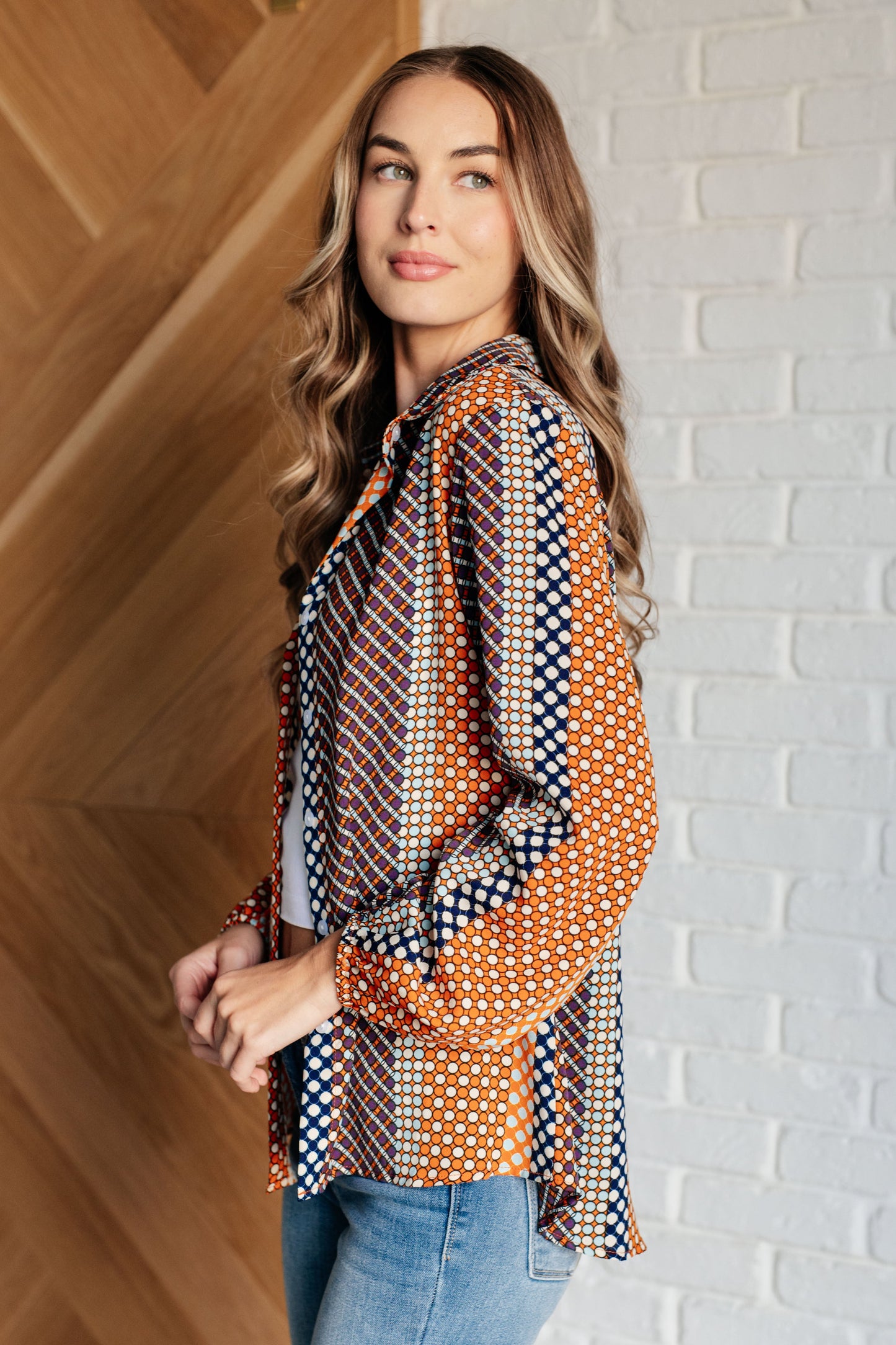 Navy, orange, brown, and pink polka dot poplin woven top with a collared neckline. Features long balloon sleeves with cased elastic cuffs, front button closures, and a scooped high-low hem.