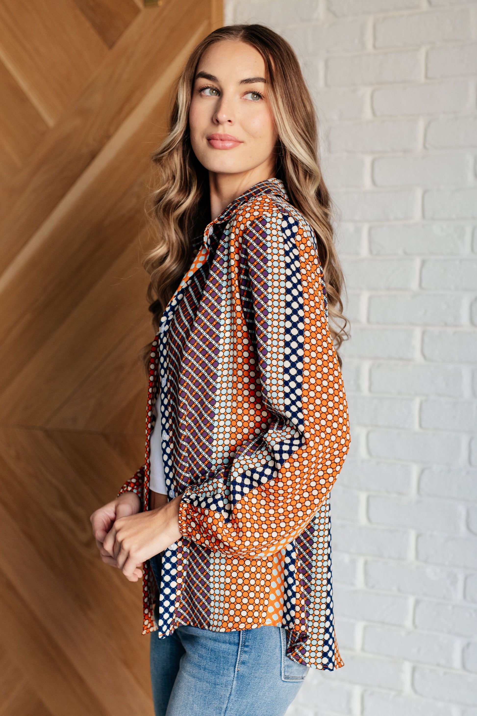 Navy, orange, brown, and pink polka dot poplin woven top with a collared neckline. Features long balloon sleeves with cased elastic cuffs, front button closures, and a scooped high-low hem.