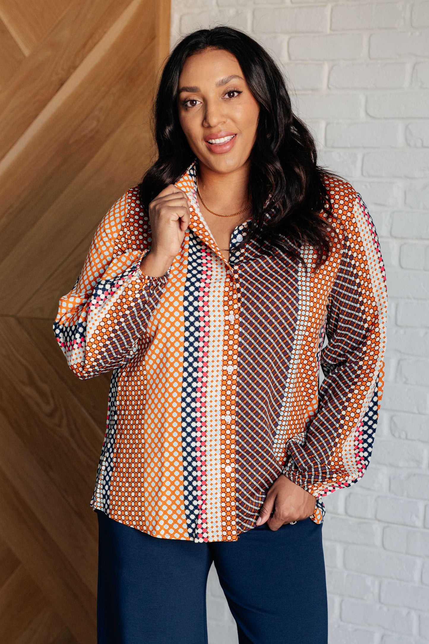 Navy, orange, brown, and pink polka dot poplin woven top with a collared neckline. Features long balloon sleeves with cased elastic cuffs, front button closures, and a scooped high-low hem.