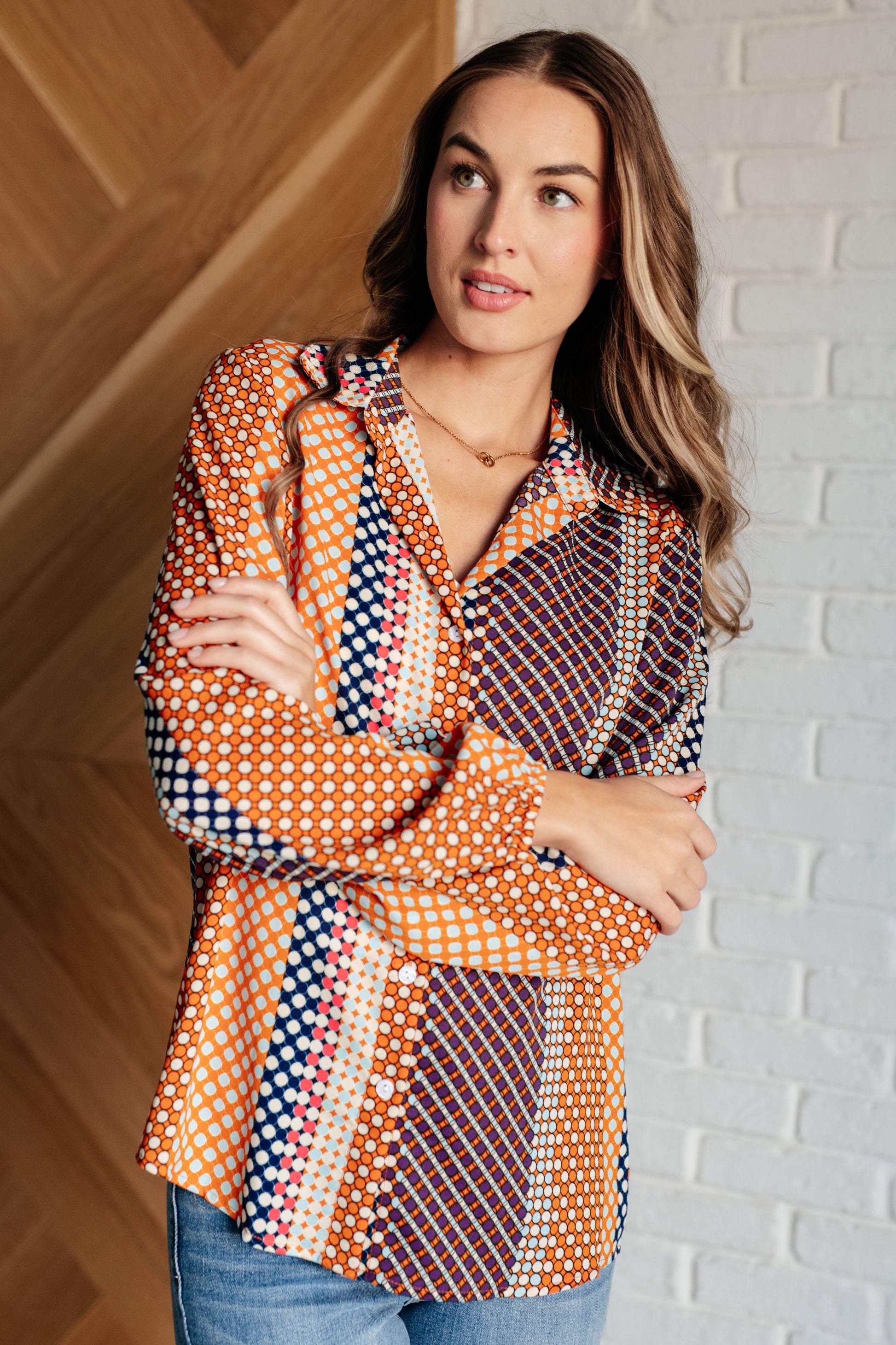 Navy, orange, brown, and pink polka dot poplin woven top with a collared neckline. Features long balloon sleeves with cased elastic cuffs, front button closures, and a scooped high-low hem.