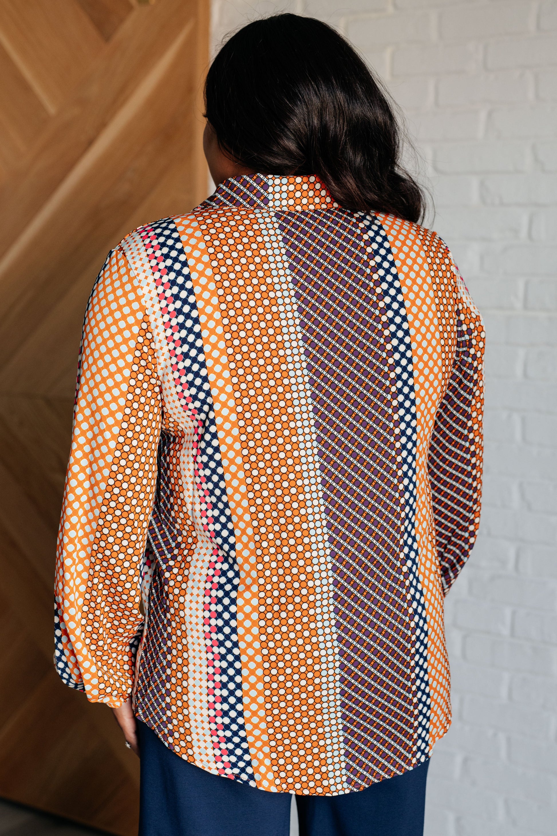 Navy, orange, brown, and pink polka dot poplin woven top with a collared neckline. Features long balloon sleeves with cased elastic cuffs, front button closures, and a scooped high-low hem.