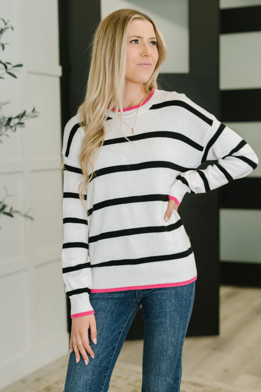 Woman wearing Daphne Striped Sweater with black-and-white stripes and pink trim, styled with jeans.
