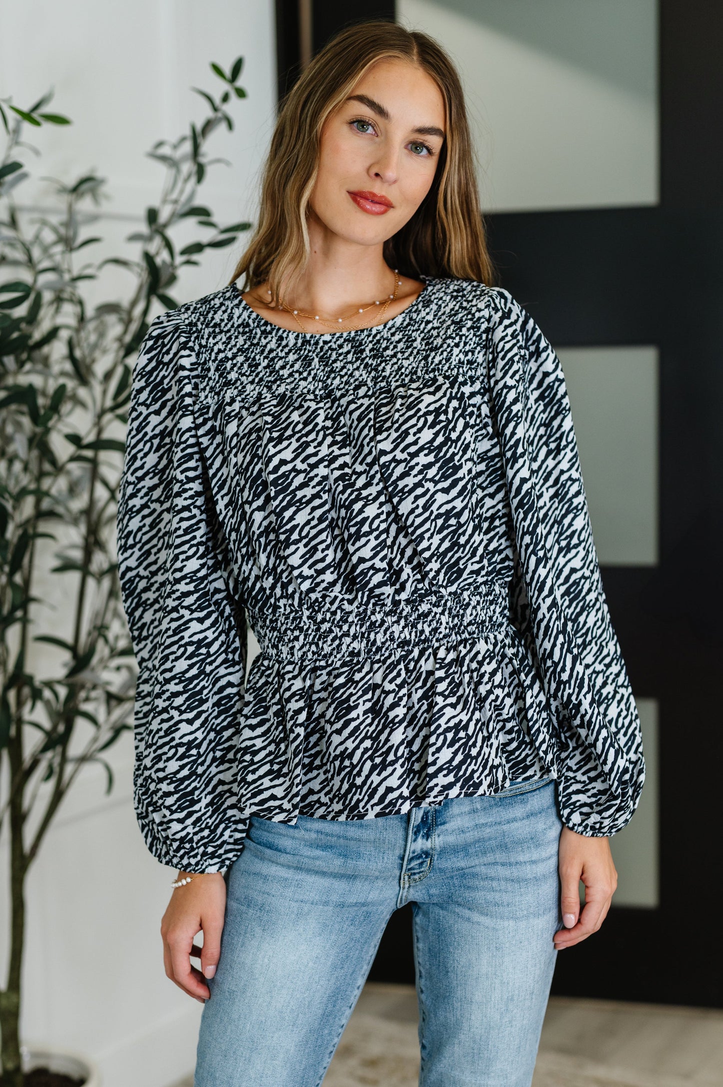 Woman wearing black peplum blouse with high neck and smocked waist, front view.