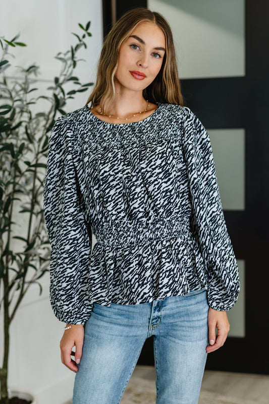 Woman wearing black peplum blouse with high neck and smocked waist, front view.