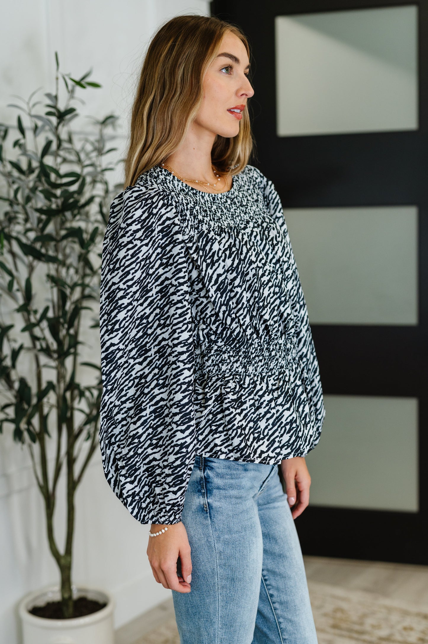 Side view of black smocked peplum blouse with long sleeves and cinched waist.