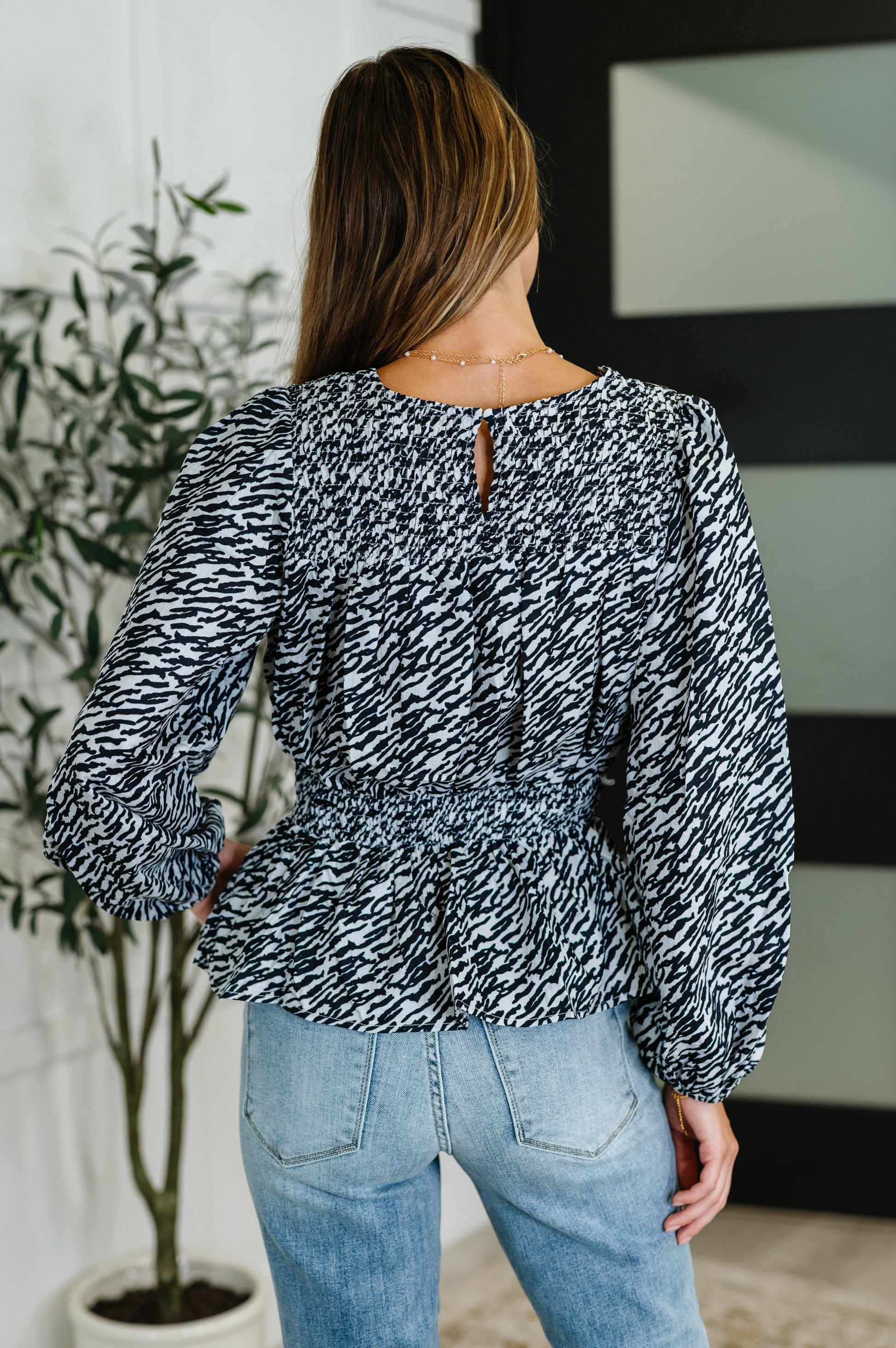 Back view of black high neck peplum blouse with keyhole closure and smocked waist.
