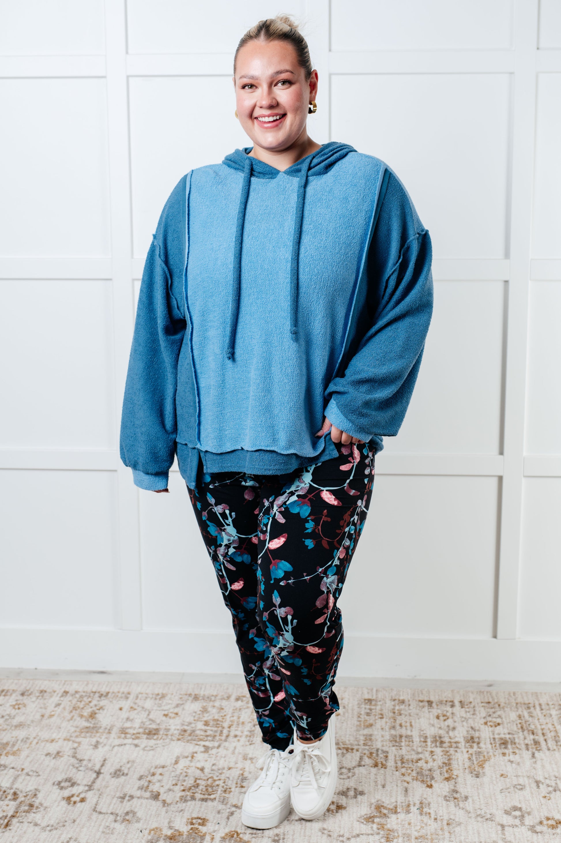 Women's blue hoodie with block color design, French Terry fabric, and hooded neckline with drawstring. Has long drop-shoulder sleeves, exposed seams, banded sleeve cuffs, and a stepped hem with side slits.