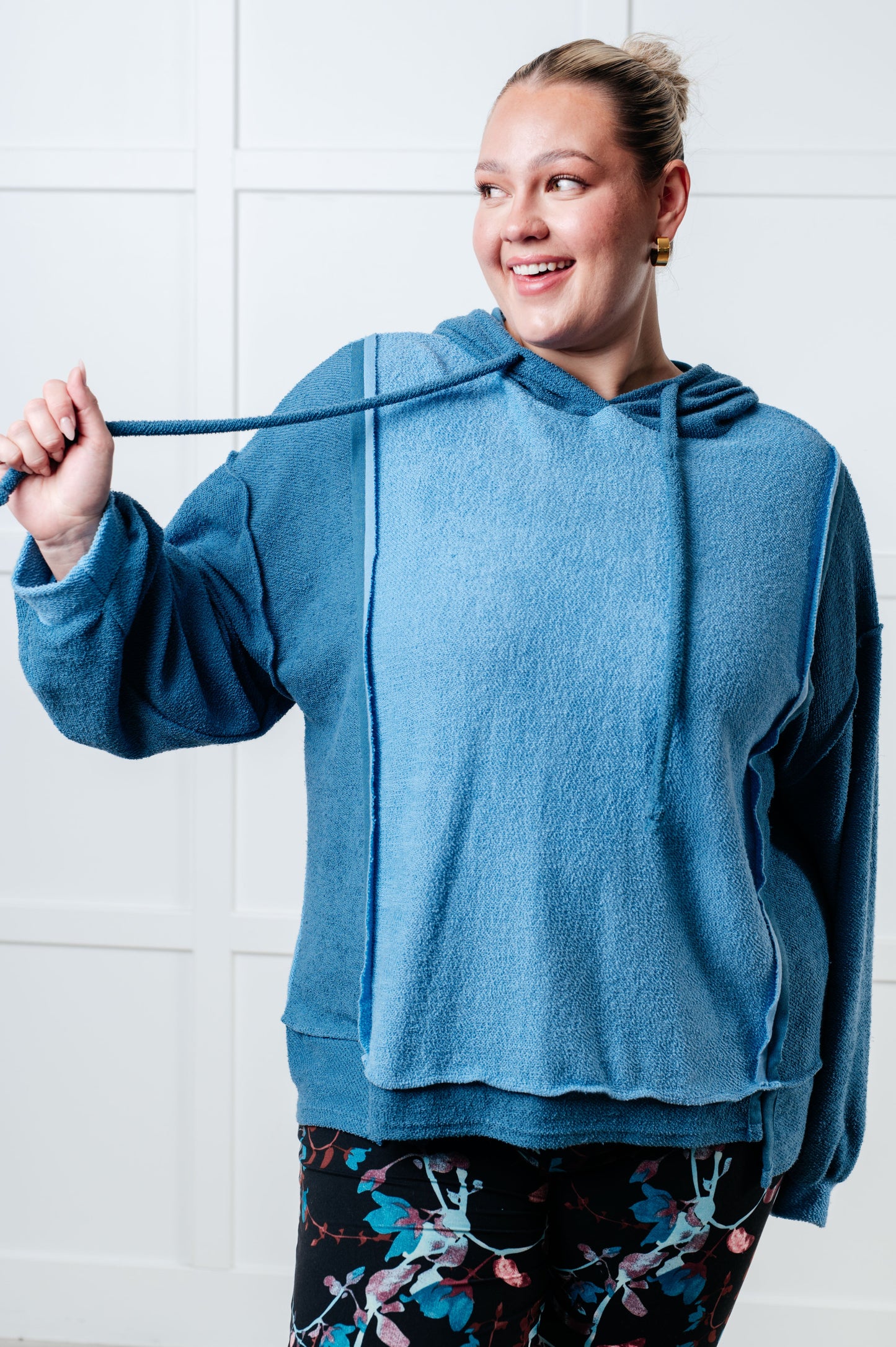 Women's blue hoodie with block color design, French Terry fabric, and hooded neckline with drawstring. Has long drop-shoulder sleeves, exposed seams, banded sleeve cuffs, and a stepped hem with side slits.