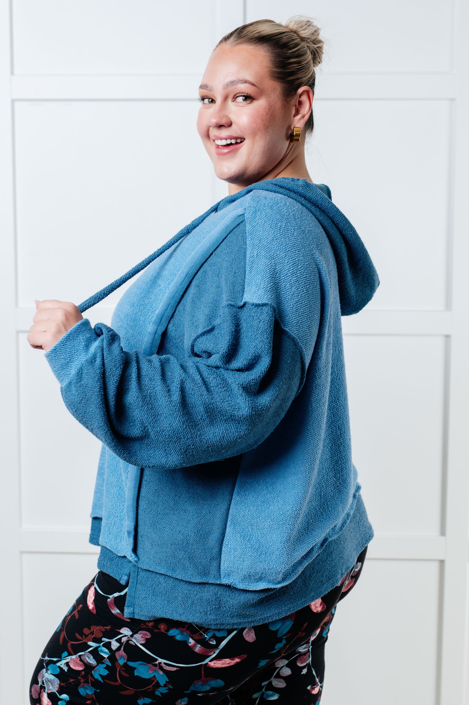 Women's blue hoodie with block color design, French Terry fabric, and hooded neckline with drawstring. Has long drop-shoulder sleeves, exposed seams, banded sleeve cuffs, and a stepped hem with side slits.