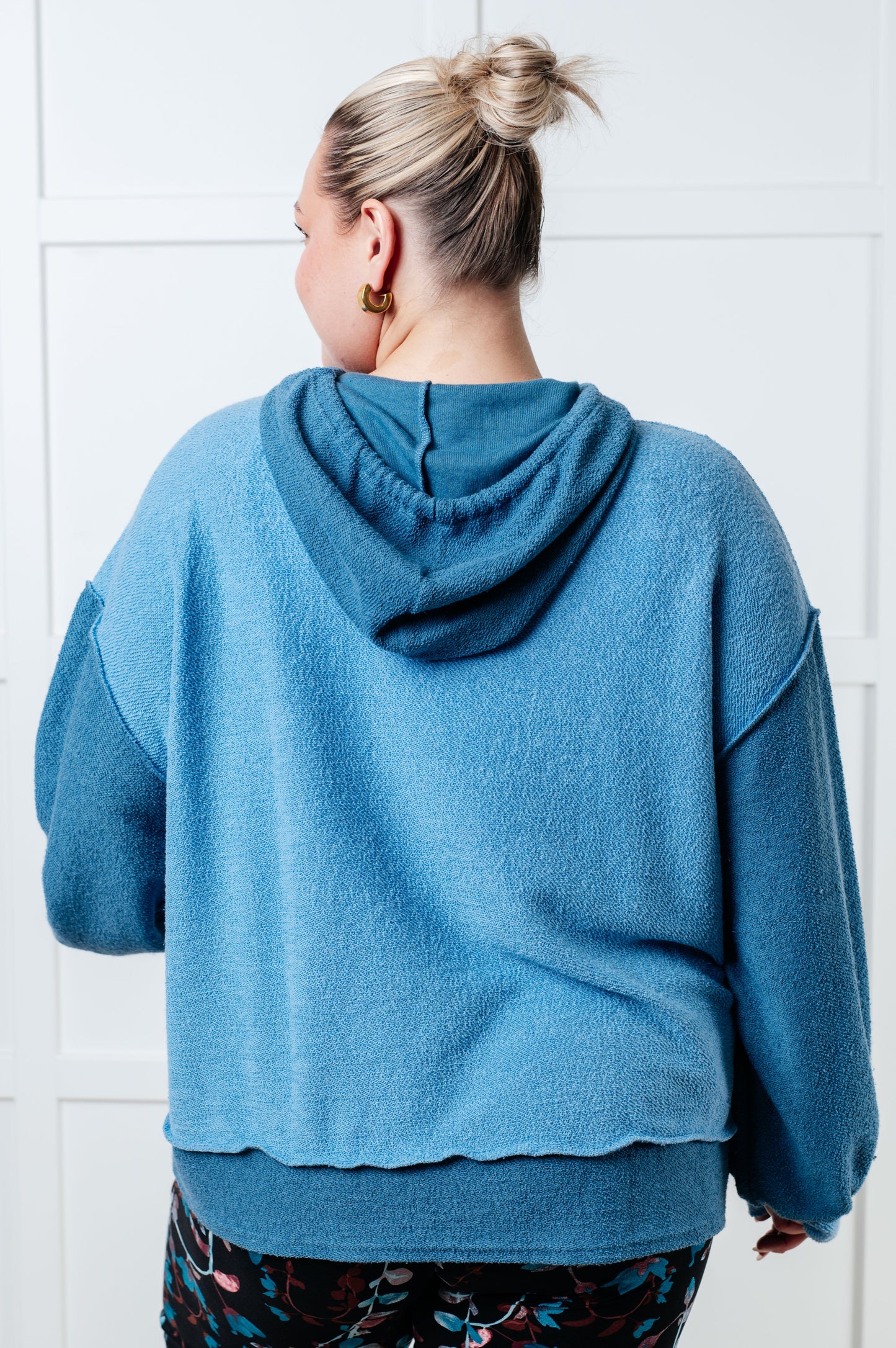 Women's blue hoodie with block color design, French Terry fabric, and hooded neckline with drawstring. Has long drop-shoulder sleeves, exposed seams, banded sleeve cuffs, and a stepped hem with side slits.