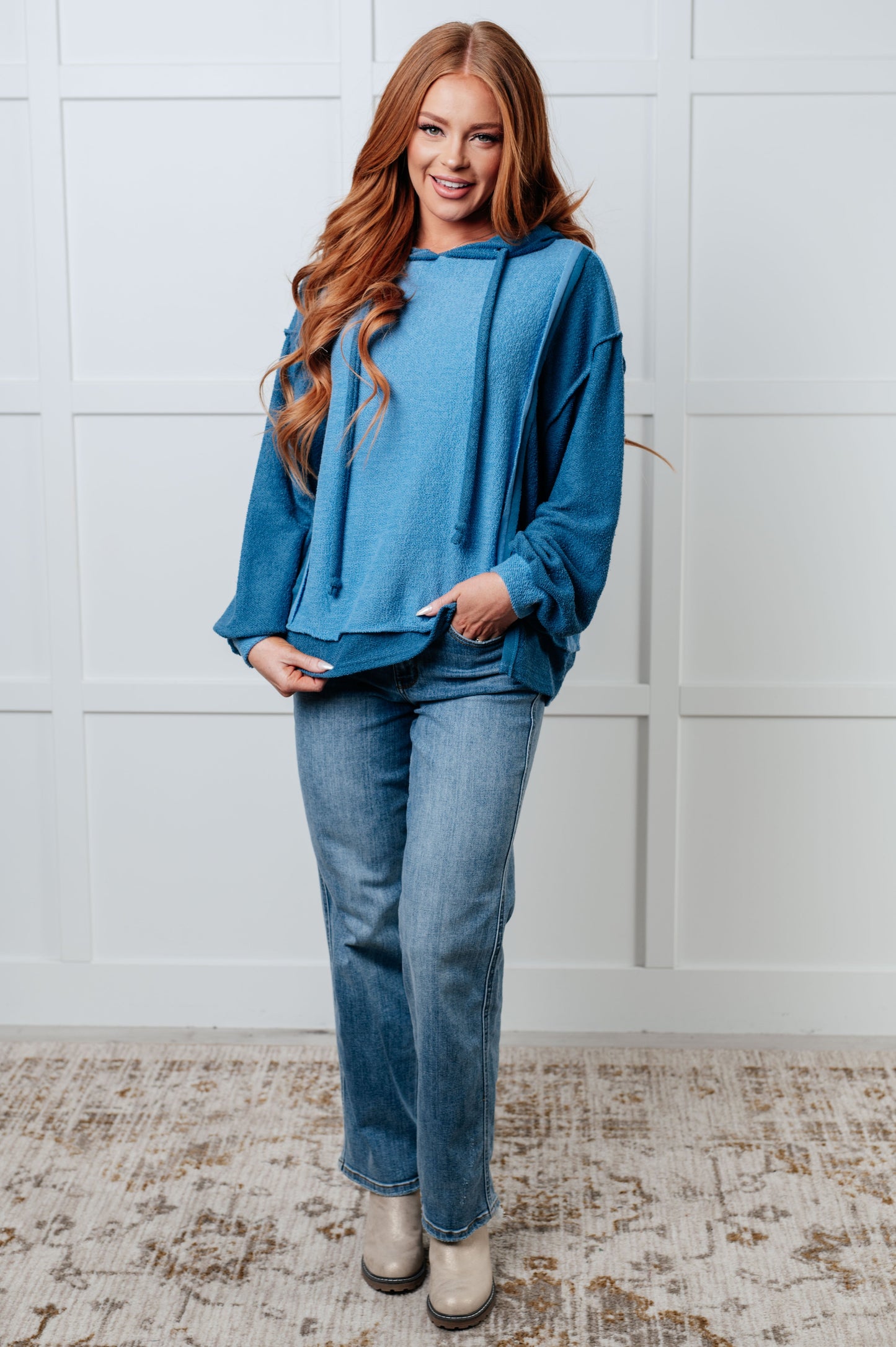 Women's blue hoodie with block color design, French Terry fabric, and hooded neckline with drawstring. Has long drop-shoulder sleeves, exposed seams, banded sleeve cuffs, and a stepped hem with side slits.